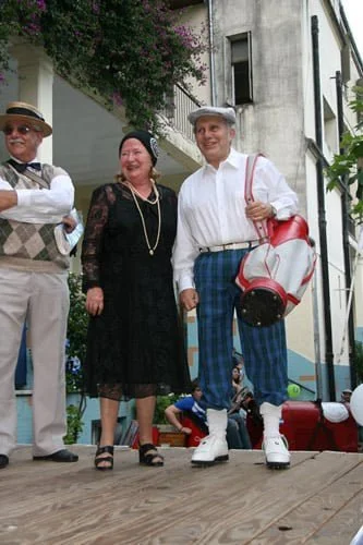 Tres personas vestidas con ropa vintage, en un escenario al aire libre, sonriendo y posando para la foto.