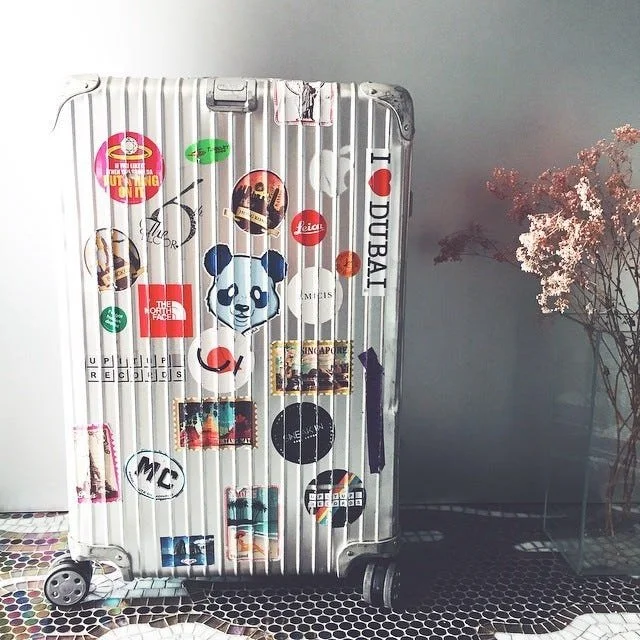 A metal effect Rimowa suitcase covered in stickers from various countries showing where the owner has traveled.