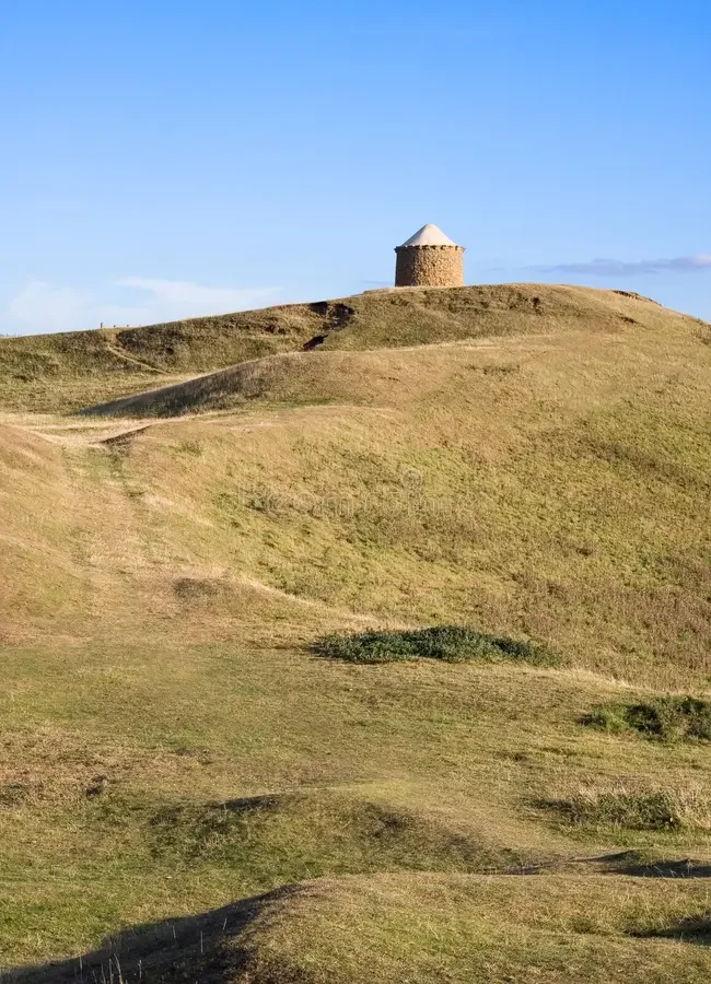 A grassy hill with a small stone tower at the top under a clear blue sky.