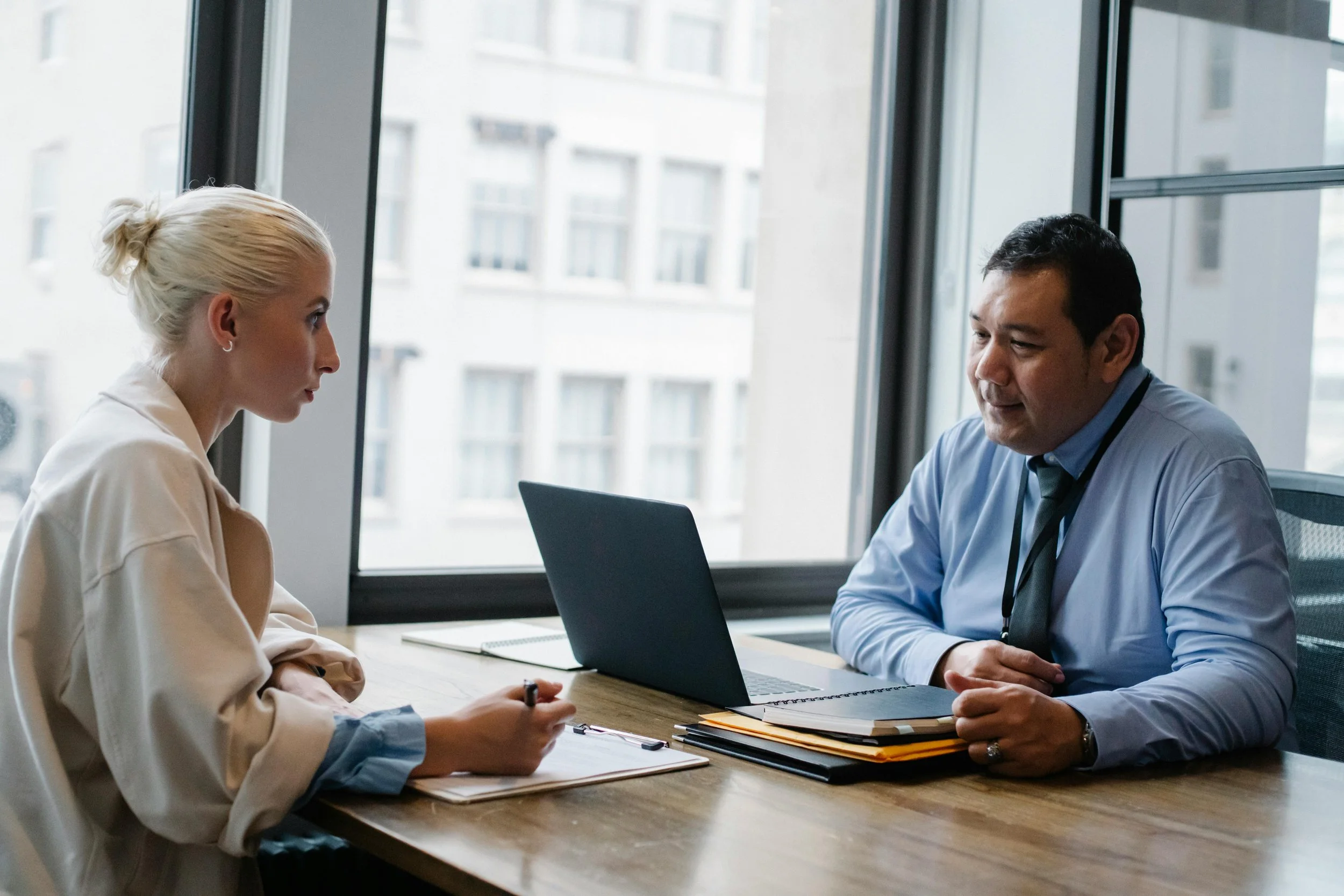 A woman and a man having a discussion in an office with large windows.
