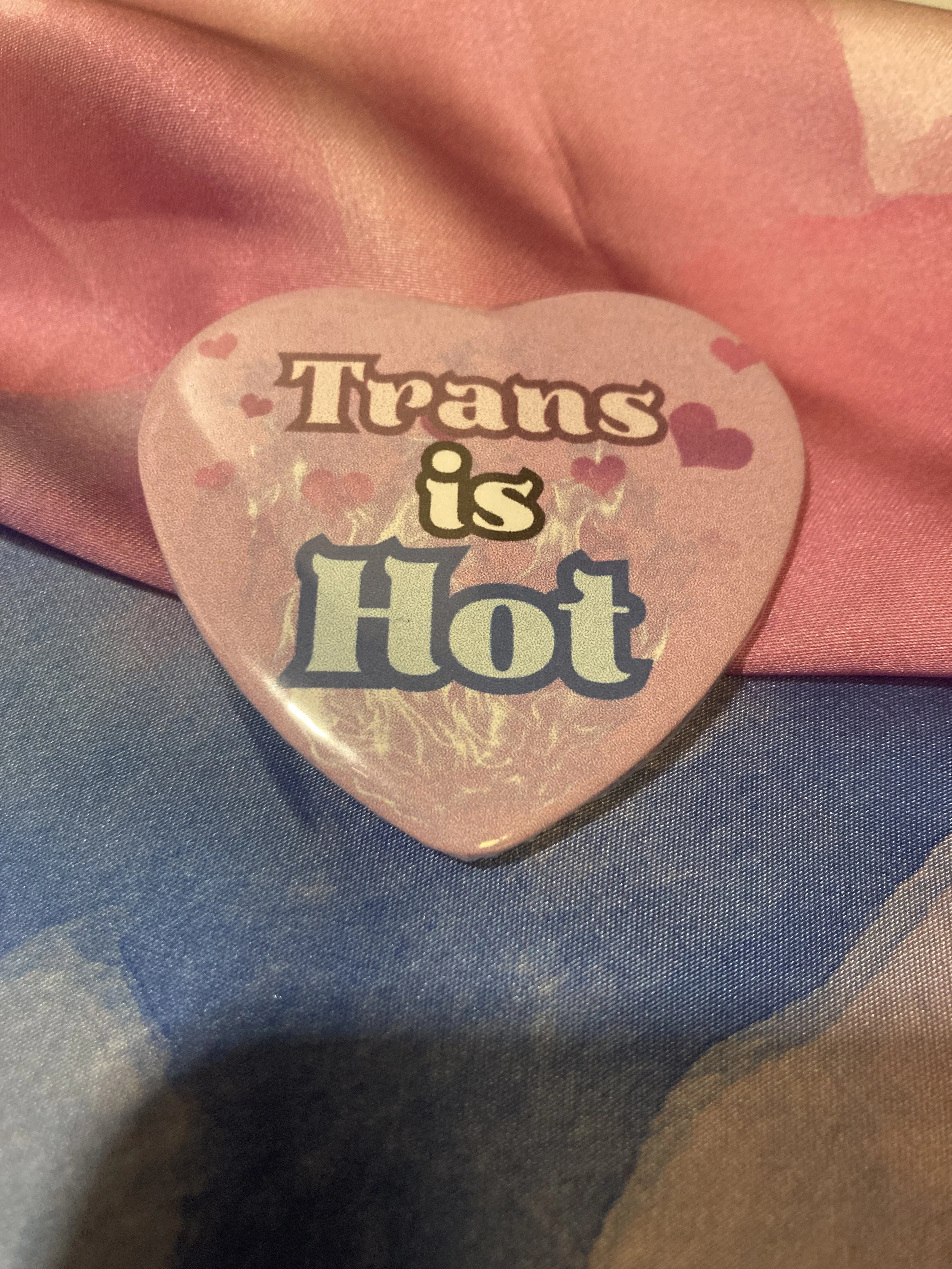 Heart shaped button that says Trans is Hot with a pink heart/flame background