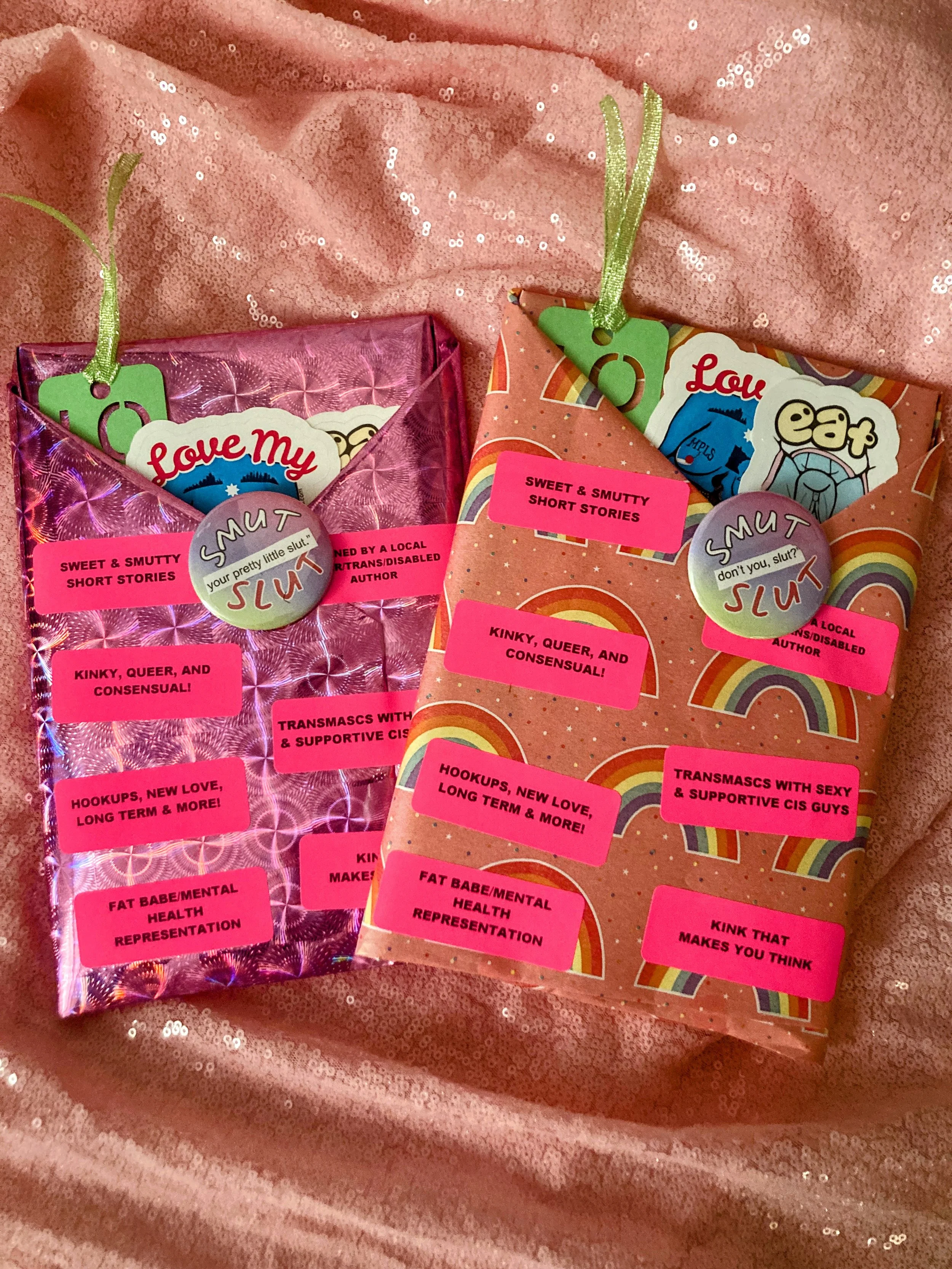 Two books wrapped in pink paper with pink labels detailing what's inside. Bookmarks and stickers are stuffed into the pocket and a button is pinned to the front.