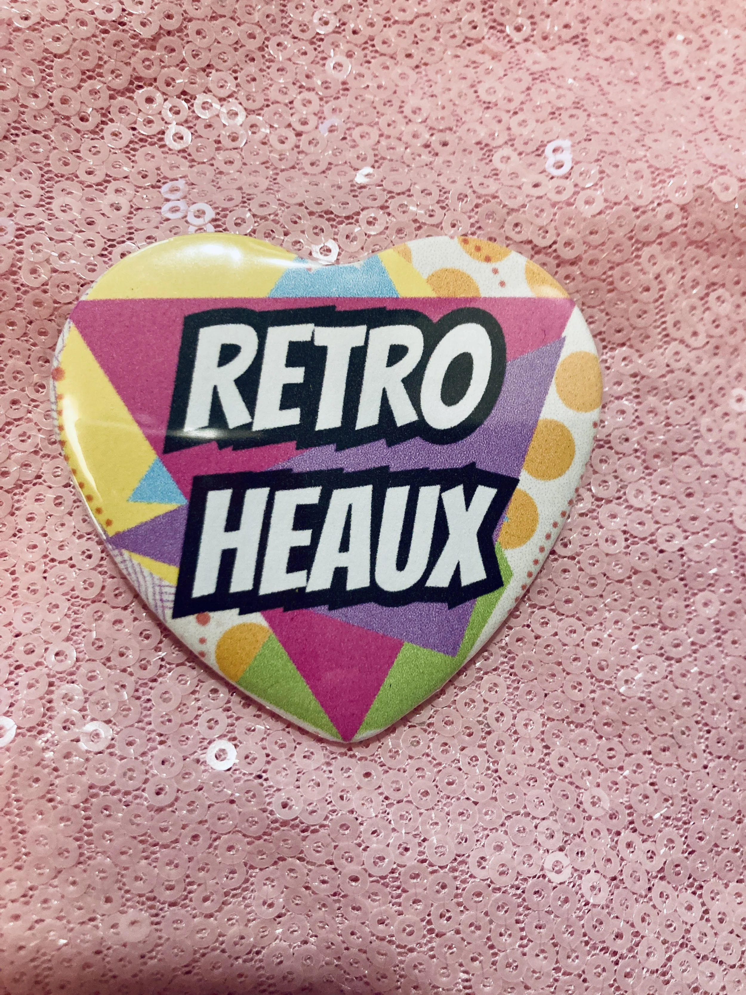 A button with a colorful 90s pattern background and the words Retro Heaux in white text with a black bordert