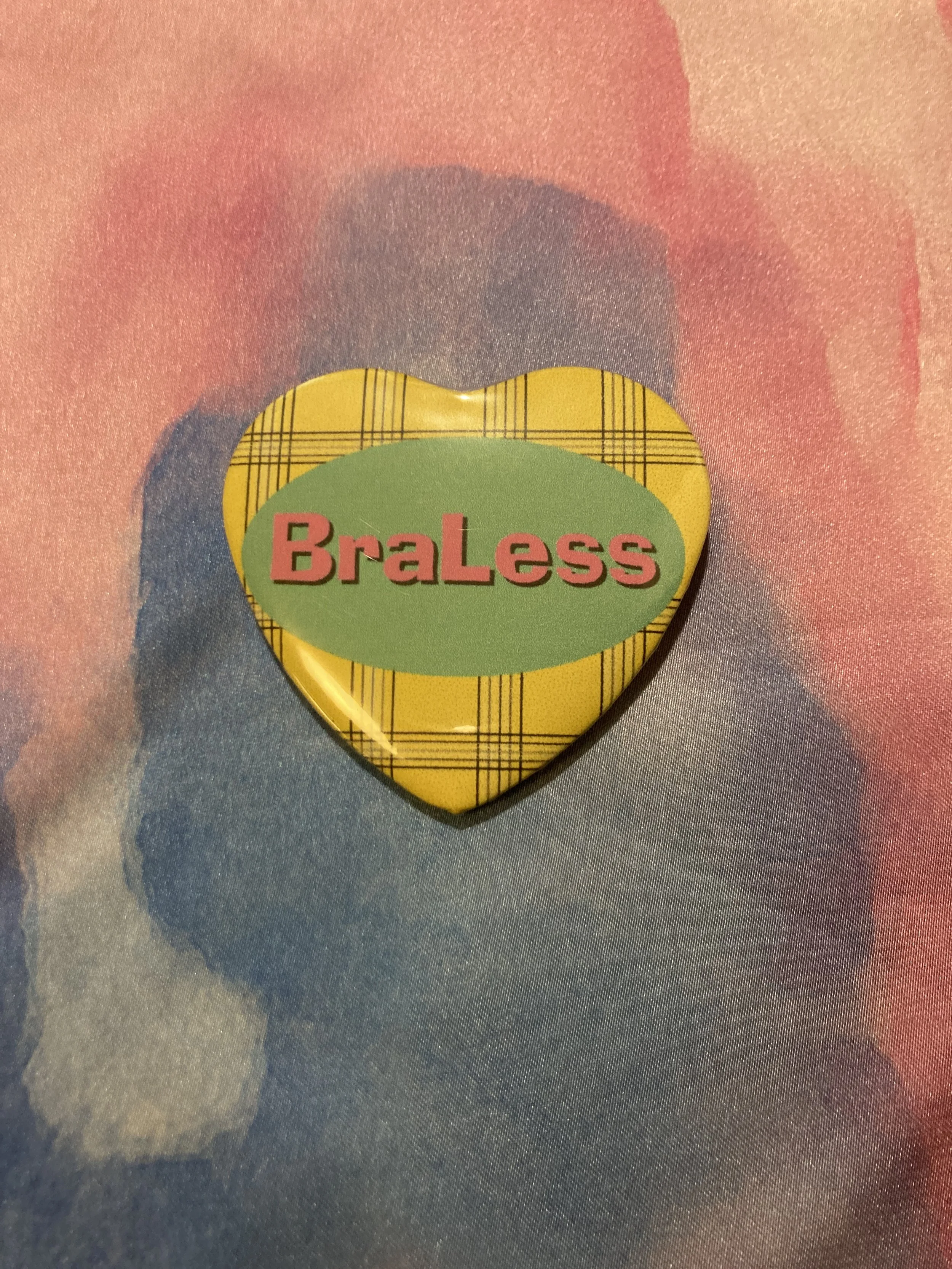 Heart shaped button that says BraLess with a yellow plaid background