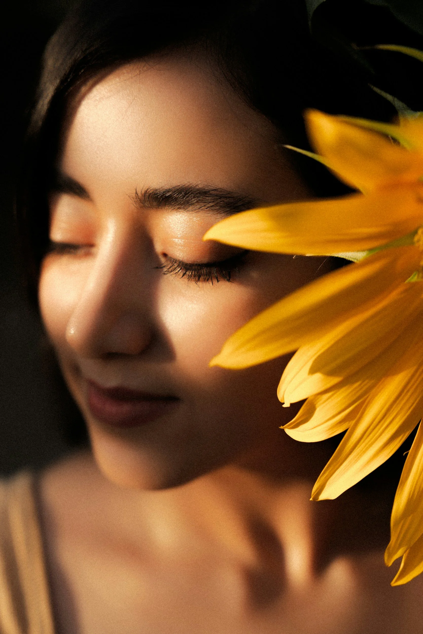 A woman with closed eyes next to a large yellow sunflower.