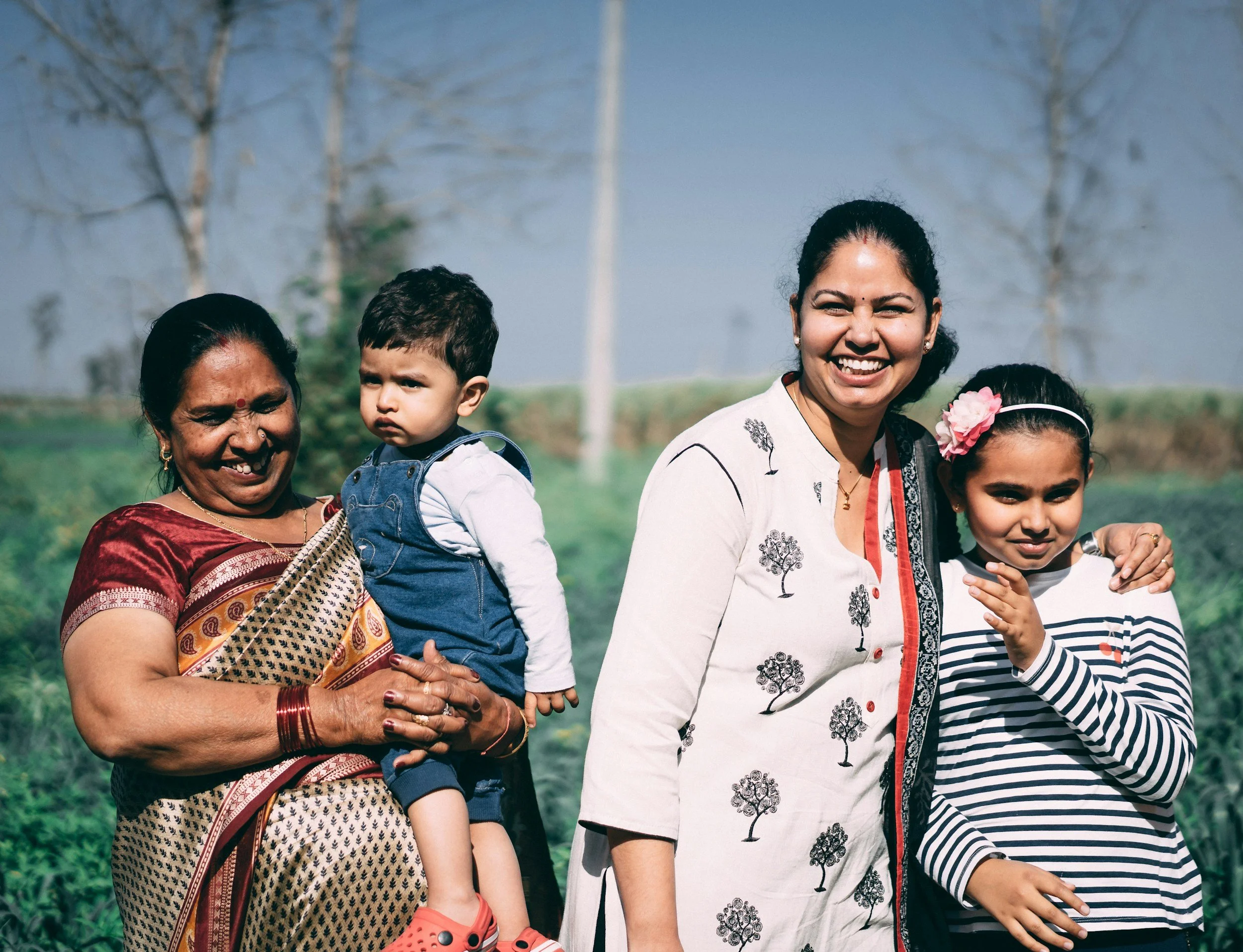 Four people of different generations outdoors smiling in a green rural setting with trees in the background.