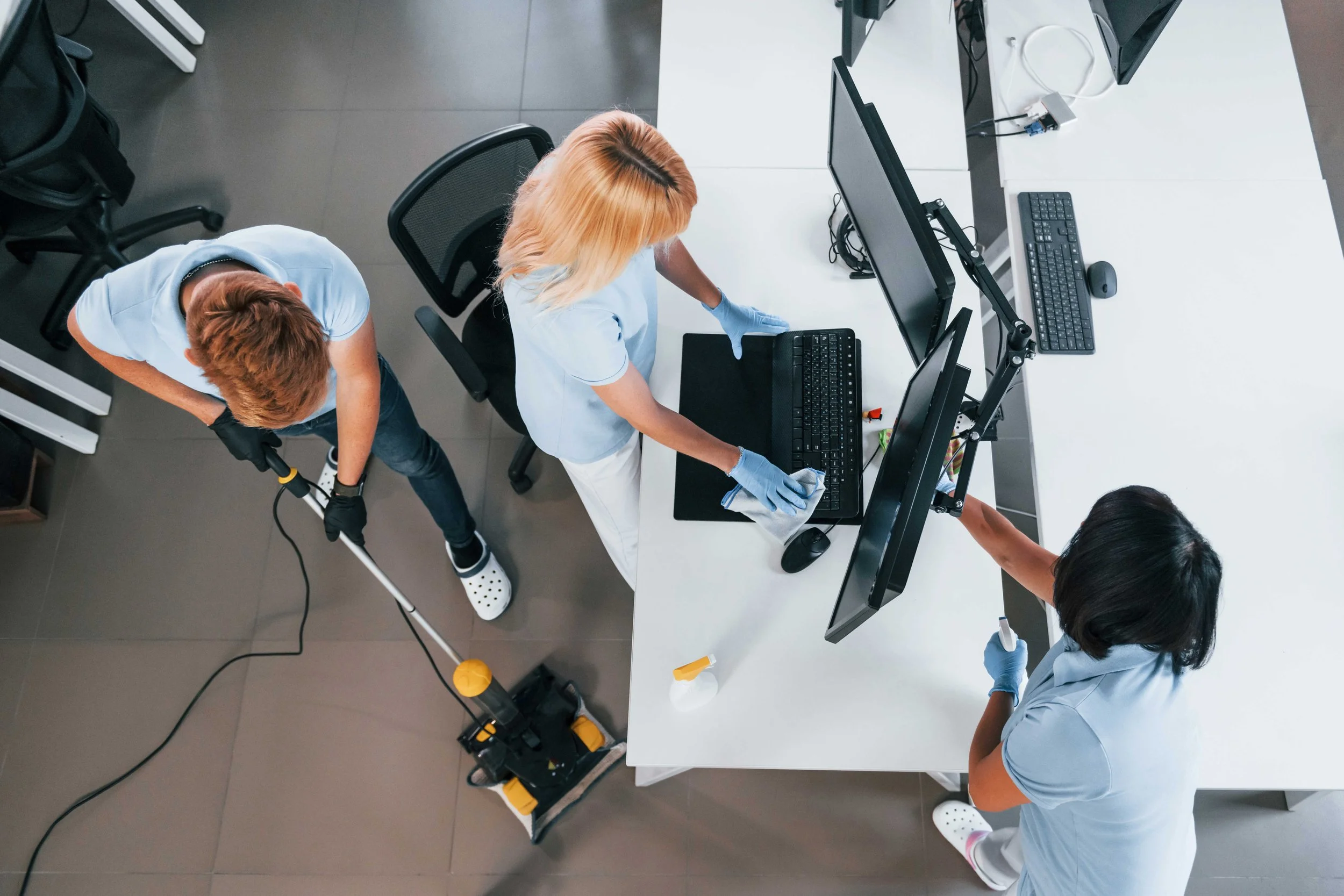 Cleaning crew disinfecting office workspace with computers and monitors.