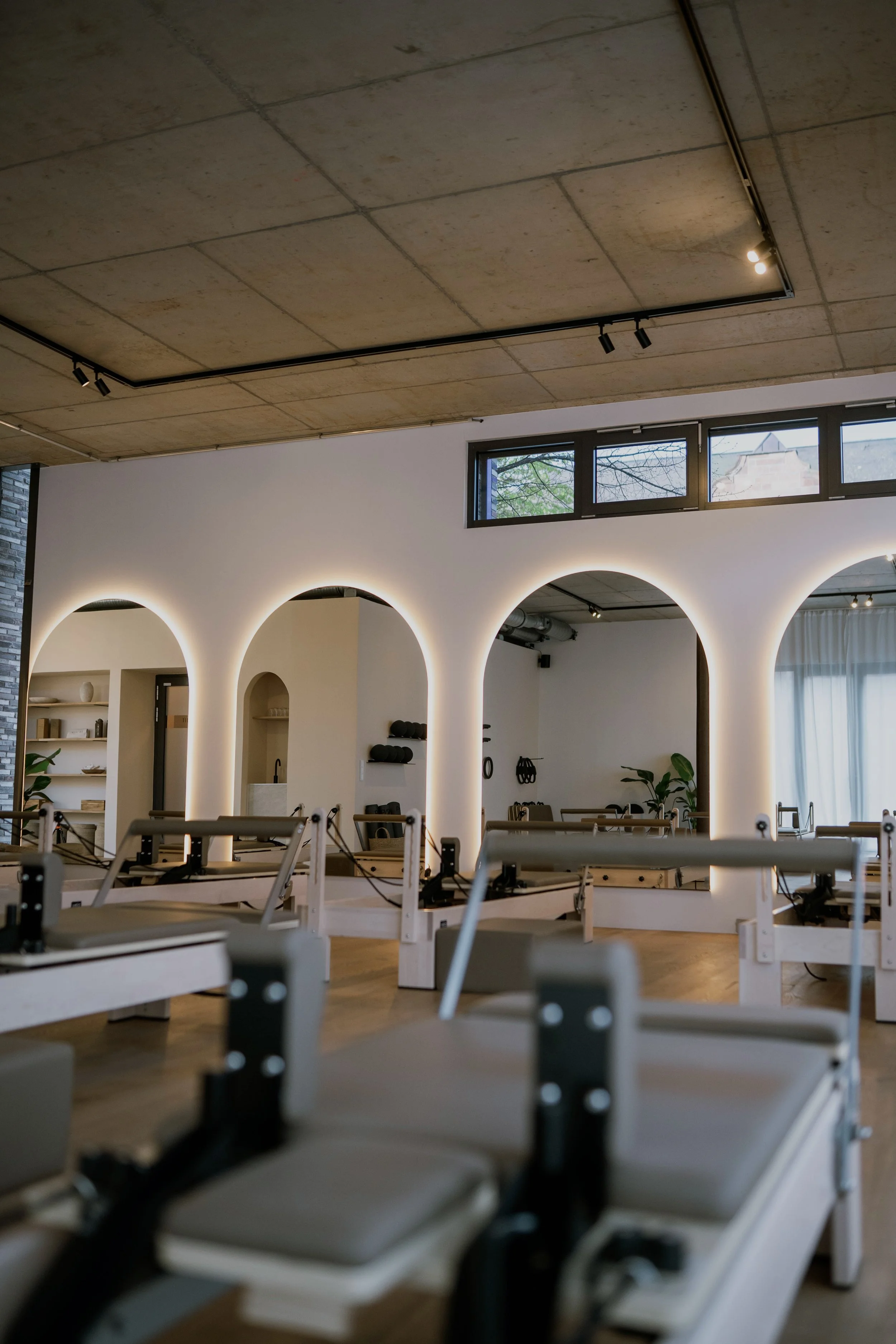 Innenansicht eines modernen Fitness-Studios mit Pilates- oder Yoga-Geräten, weißen arches mit Beleuchtung und großen Fenstern