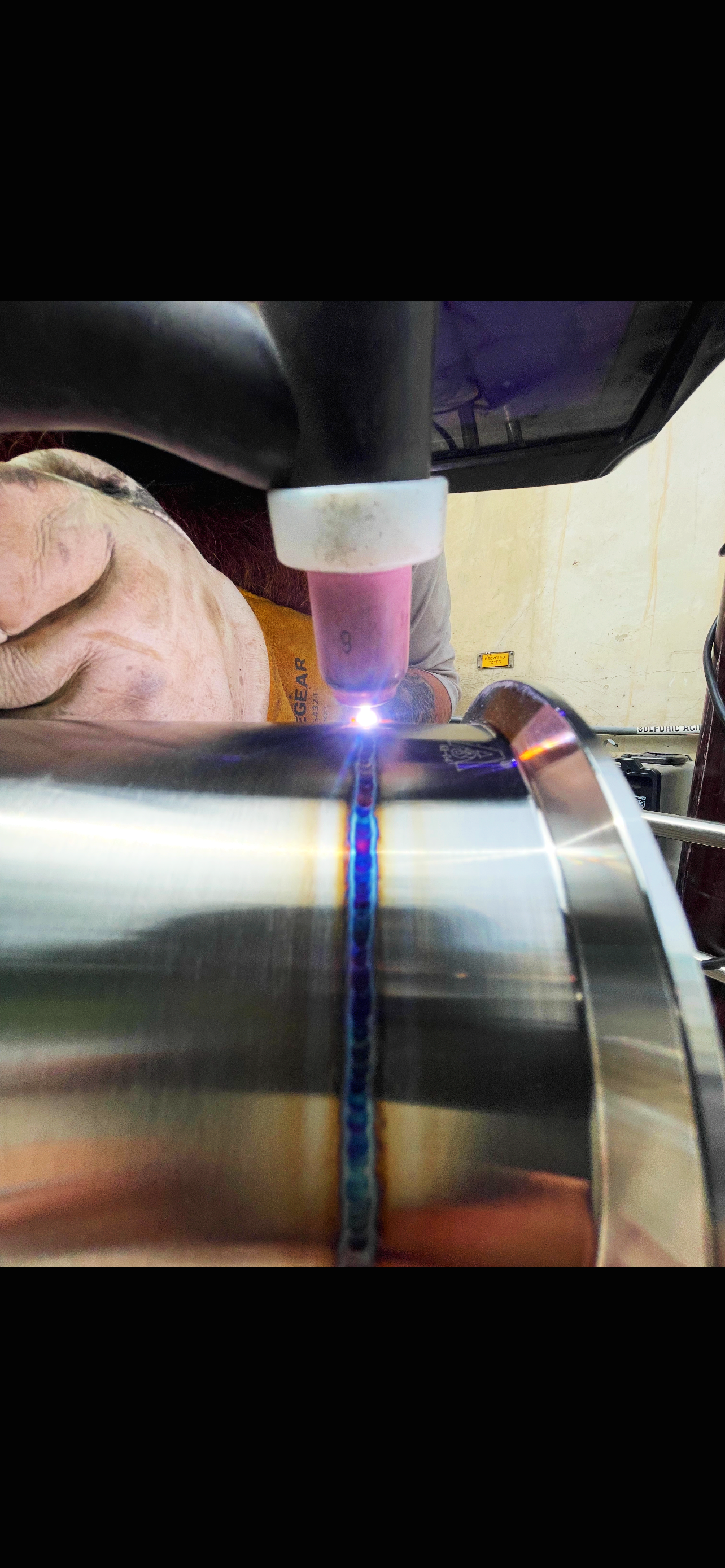 A person welding a metal pipe with a bright blue and yellow light from the welding torch.