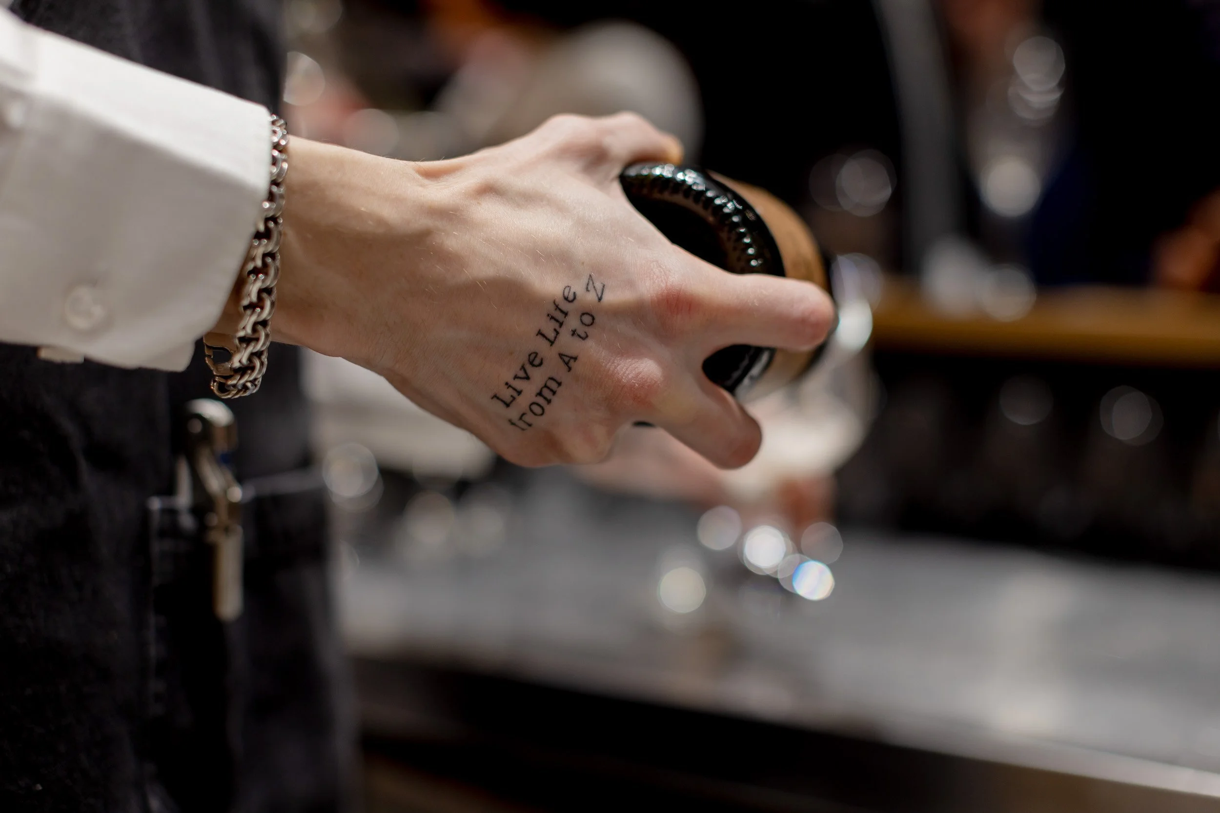 Nahaufnahme einer Hand, die ein Glas hält. Auf der Hand ist ein Tattoo.