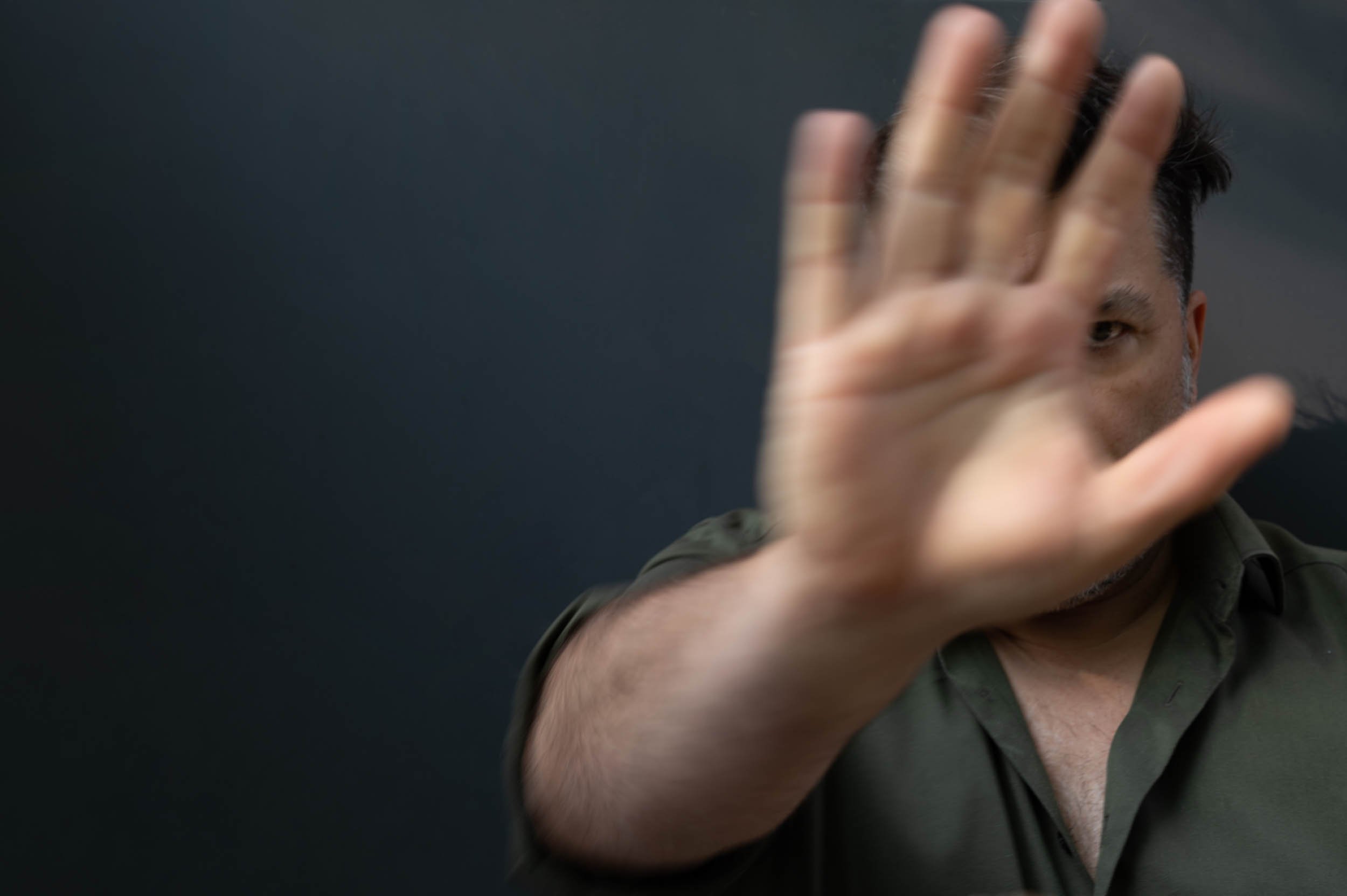 Nahaufnahme eines Mannes, der seine Hand vor seinem Gesicht hält, vor dunklem Hintergrund.