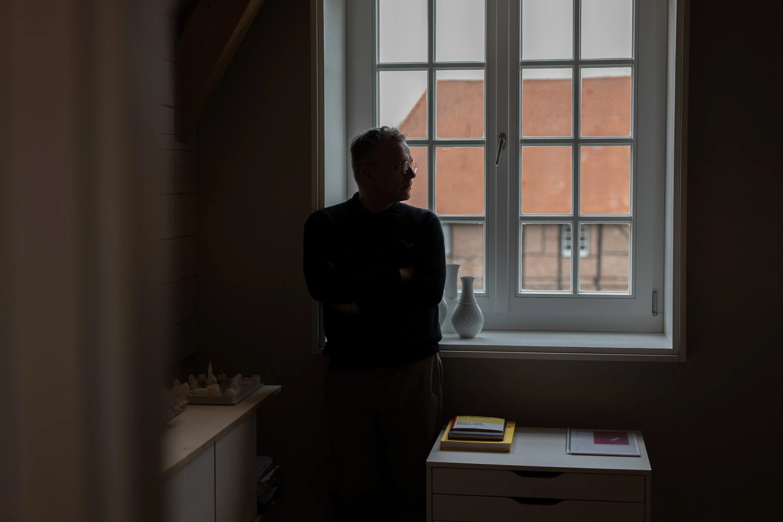 Ein Mann steht in einem dunklen Raum vor einem Fenster mit Blick nach draußen, die Silhouette ist sichtbar. Architekt.