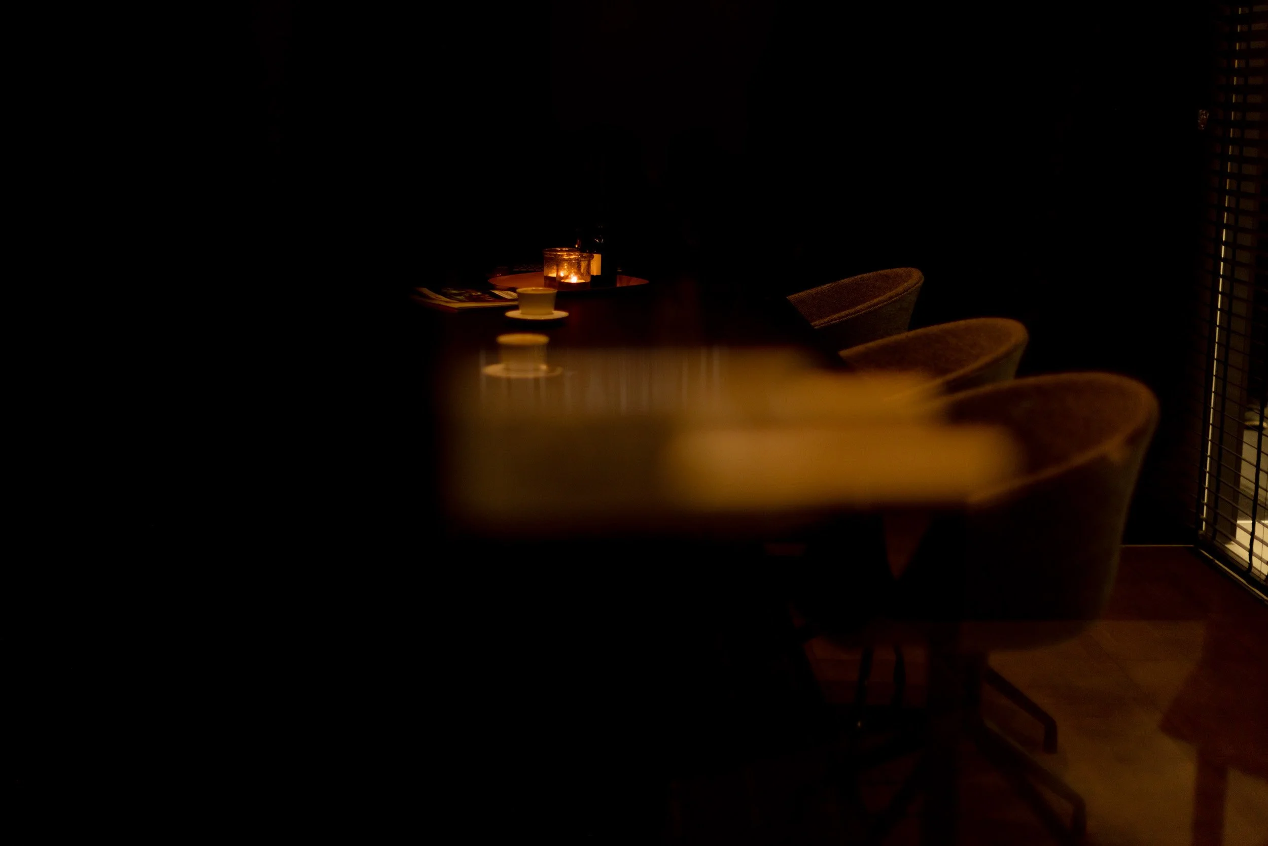 Gemütlich beleuchteter Esstisch mit Kerzen und Stühlen in einem dunklen Raum.