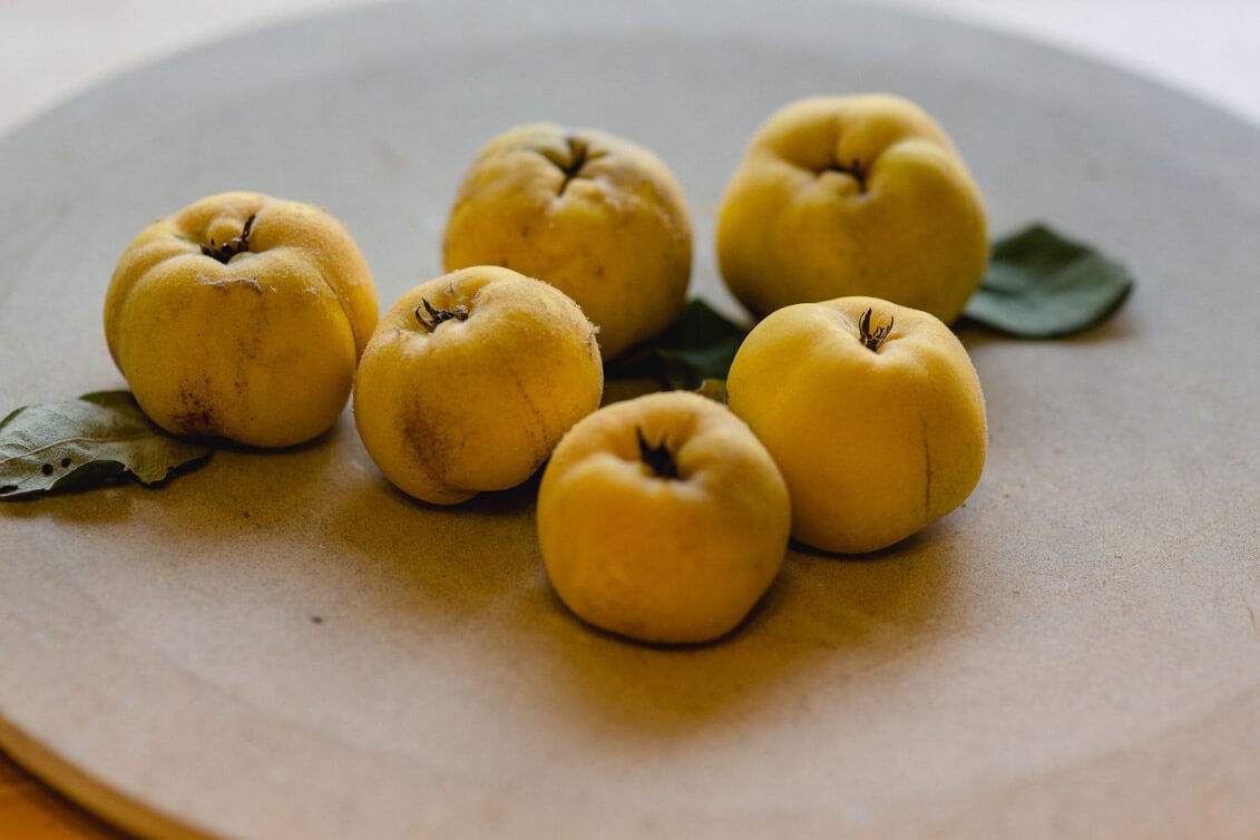 Sechs pflückreife Quitten auf einem runden, grauen Teller mit einigen grünen Blättern.