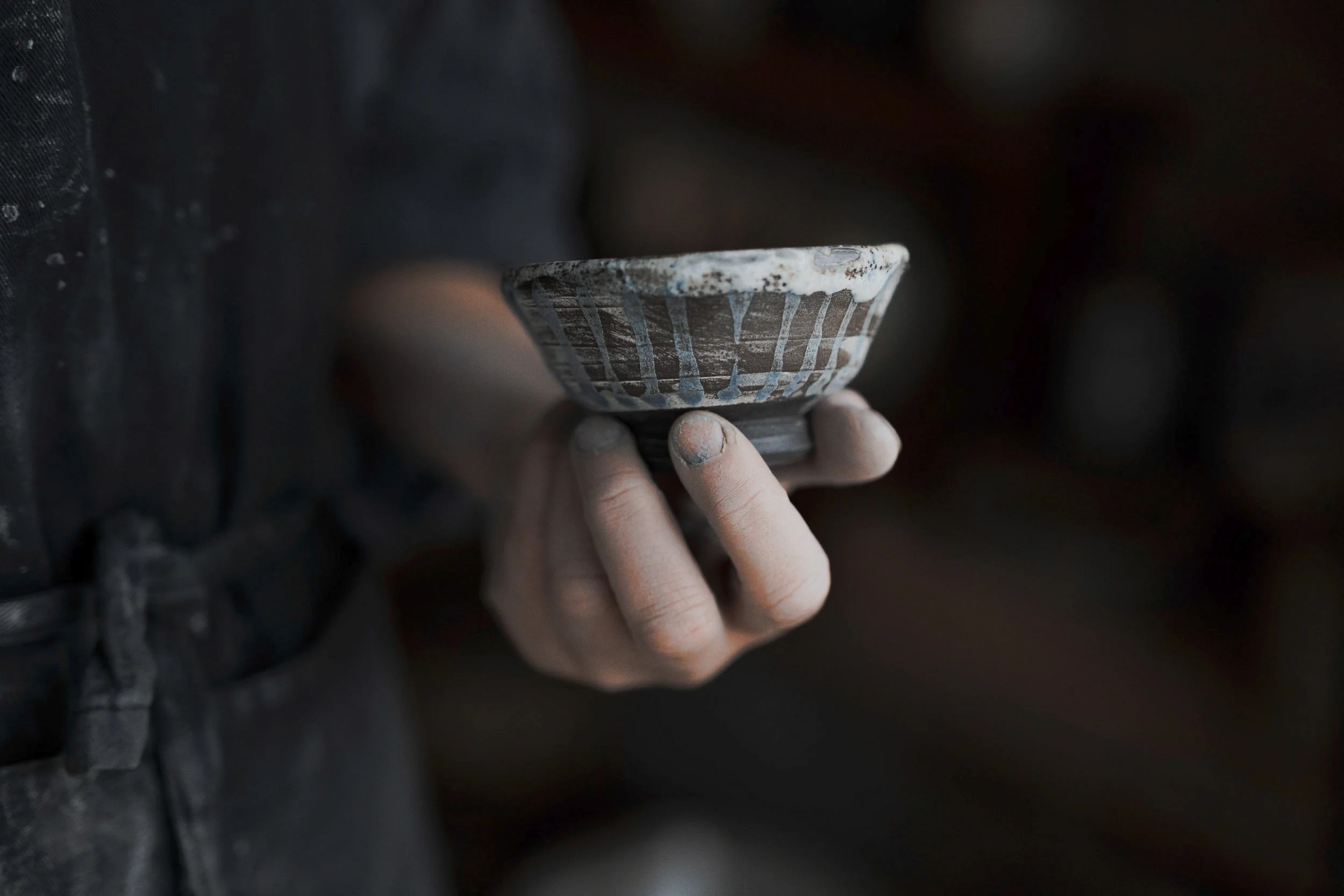 Hand hält eine gebrauchte, bemalte Keramikschale mit blauer und brauner Verzierung.