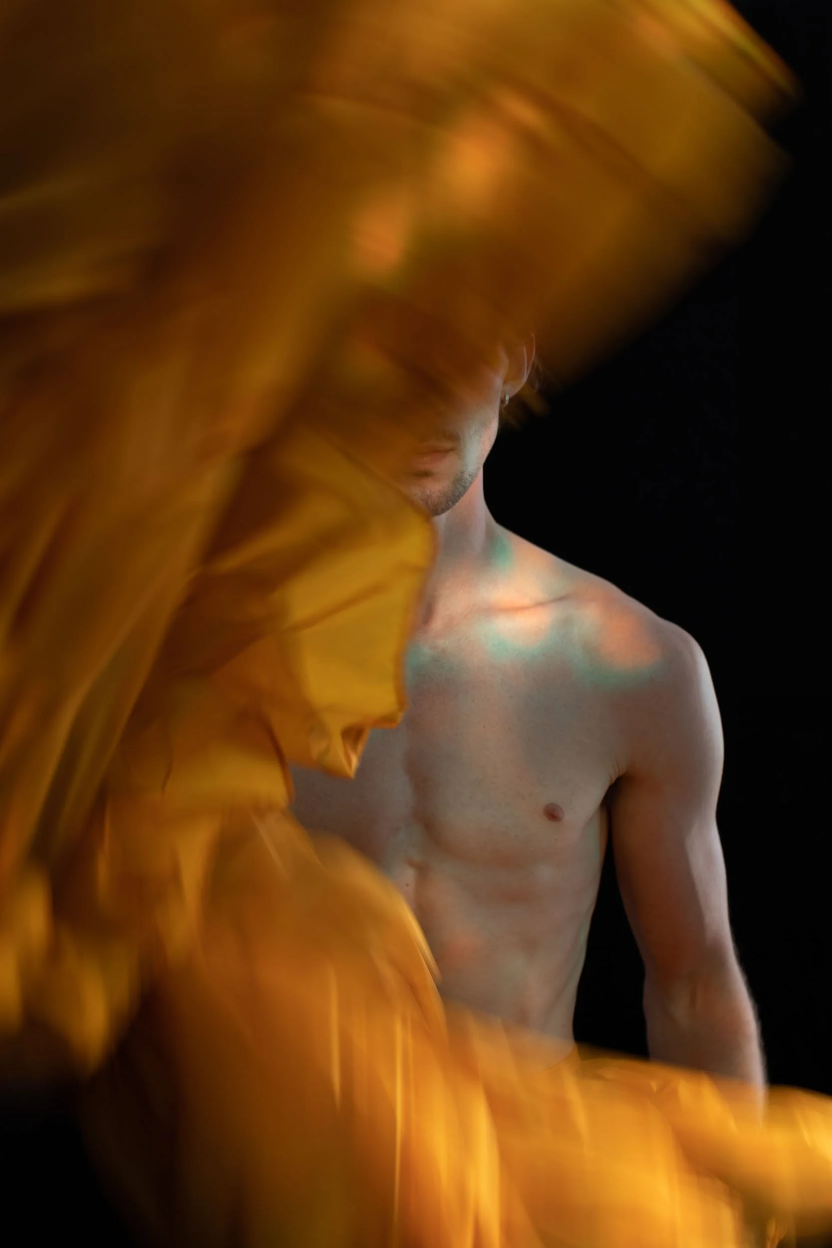 Ein junger Mann , teilweise verdeckt durch einen gelben Stoff oder Vorhang, vor einem schwarzen Hintergrund.