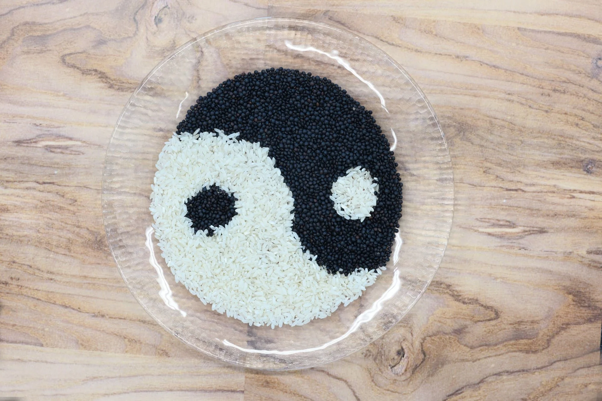 Ein Teller mit weißen und schwarzen Reiskörnern, die in einem Yin-Yang-Symbol angeordnet sind.