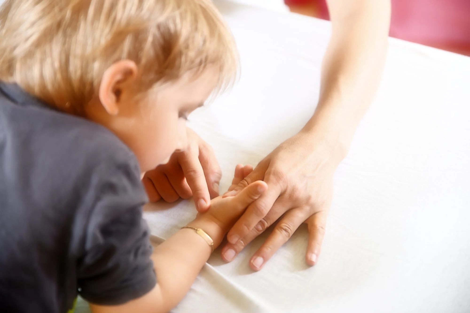Ein Kind hält die Hand einer erwachsenen Person auf einem weißen Bettlaken.