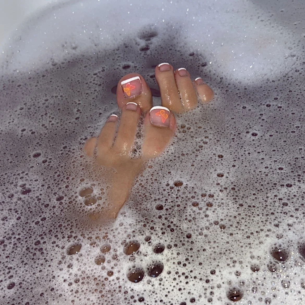 Hand with decorated nails submerged in a foamy bubble bath.