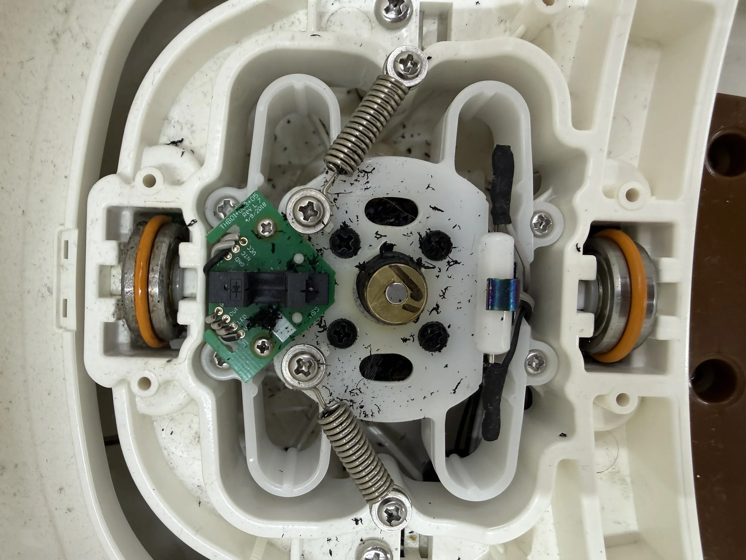 The interior of a SNOO bassinet showing wiring, springs, and circuit boards with black debris and dust.