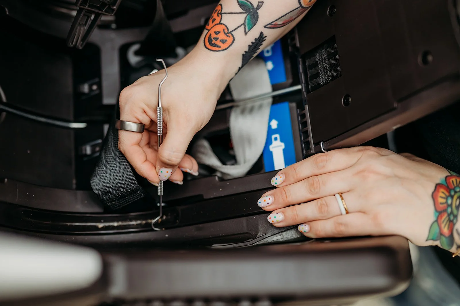 Female cleaning a car seat using a small tool, with colorful tattoos on their hands and a colorful polka dot manicure.
