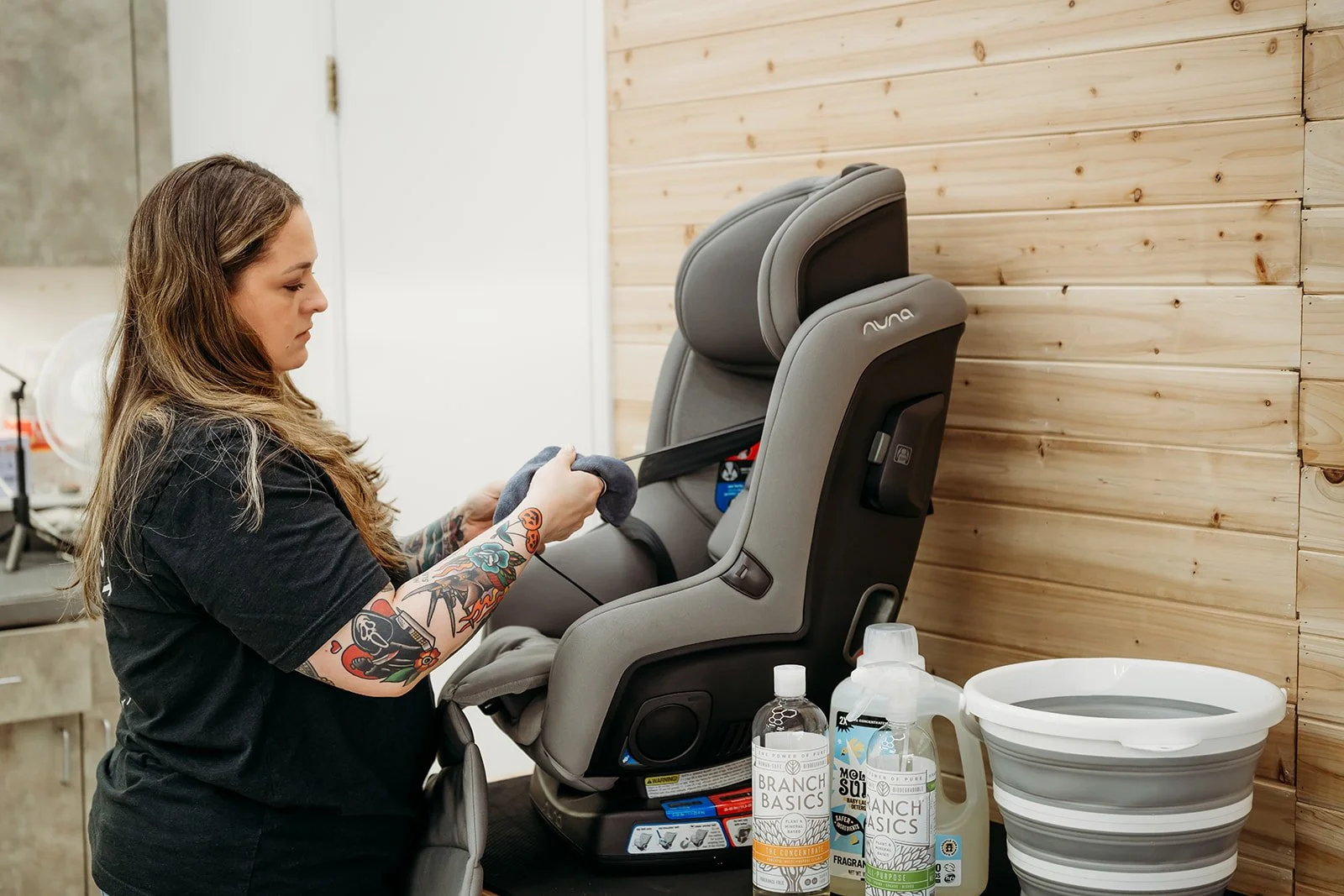 Woman with traditional arm tattoos cleaning a grey colored car seat.