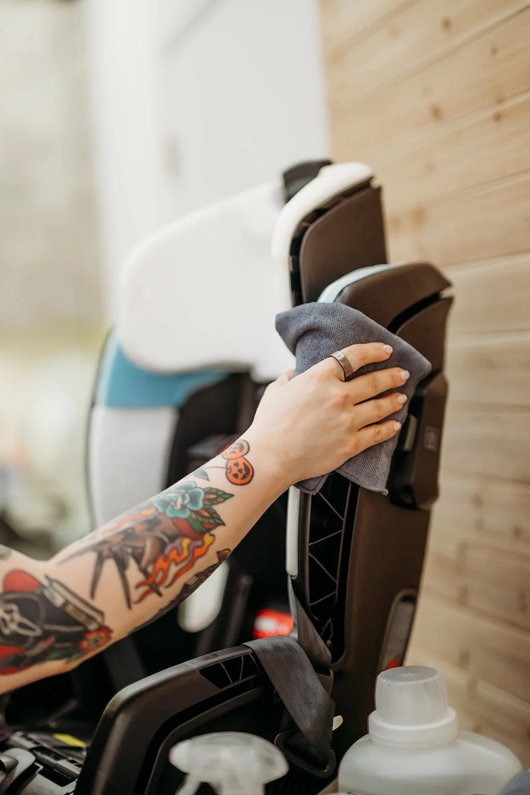 A female with a tattooed arm is wiping down a car seat with a gray cloth.