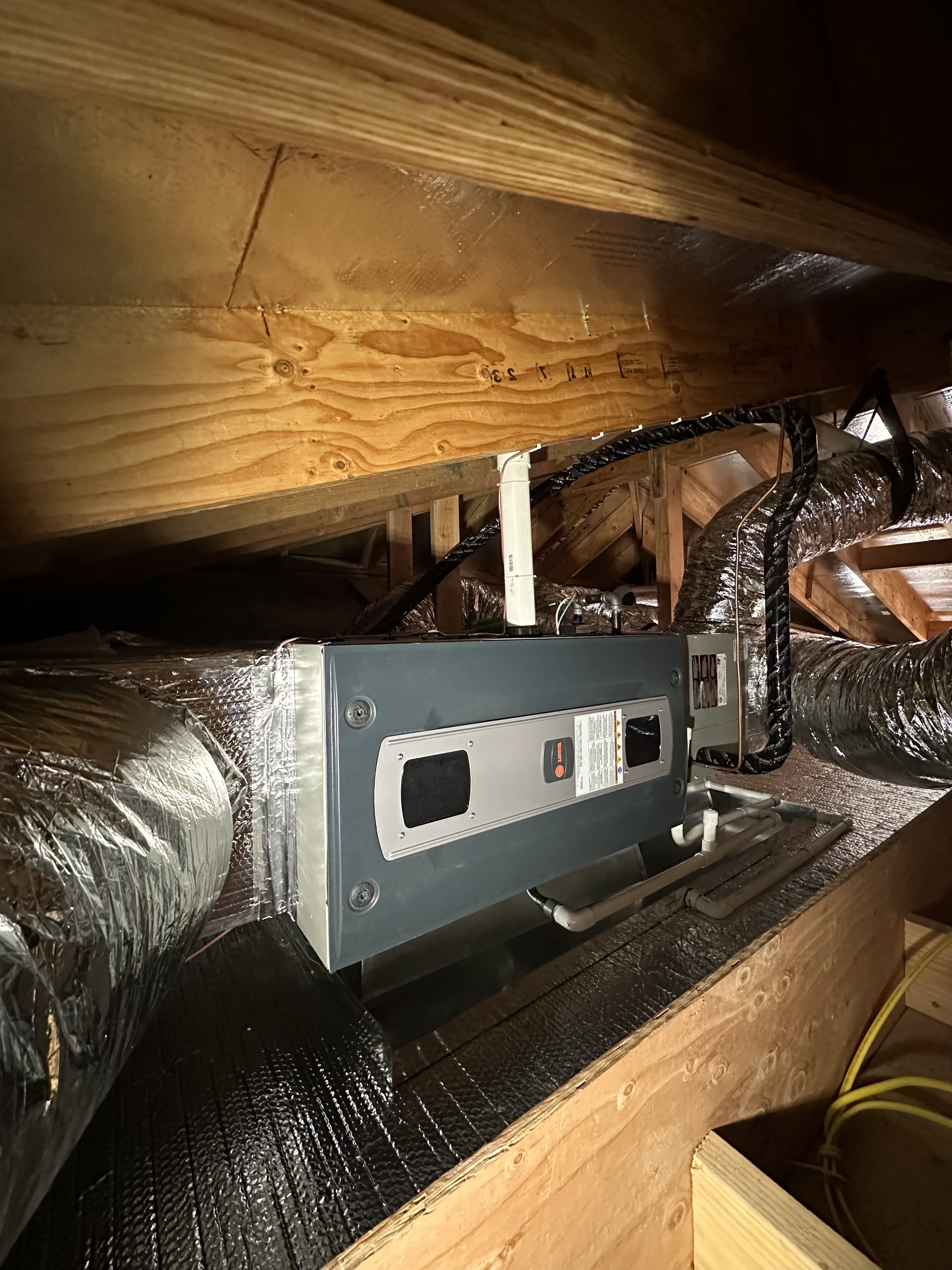 A furnace and ductwork installed in an attic space with exposed wooden framing.