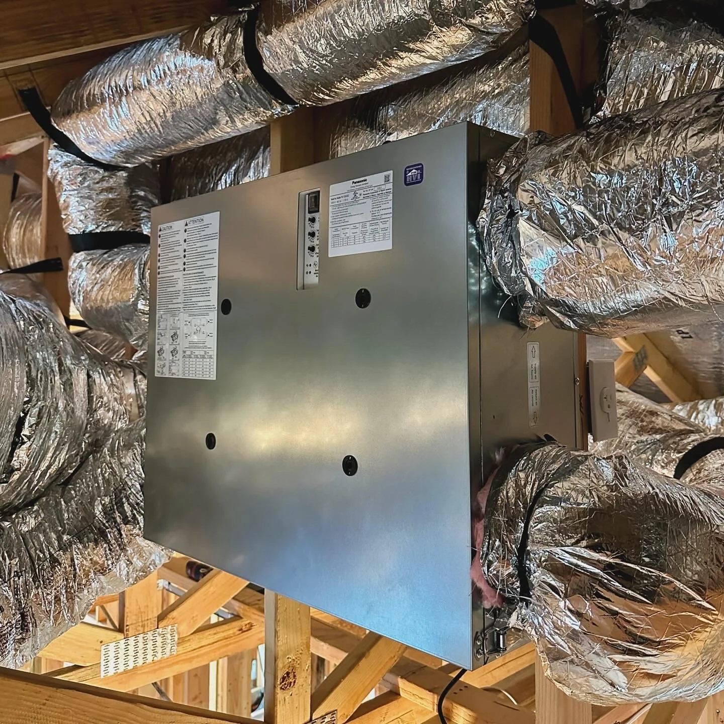 HVAC air handling unit installed within a wooden framework, surrounded by insulated flexible ducts.