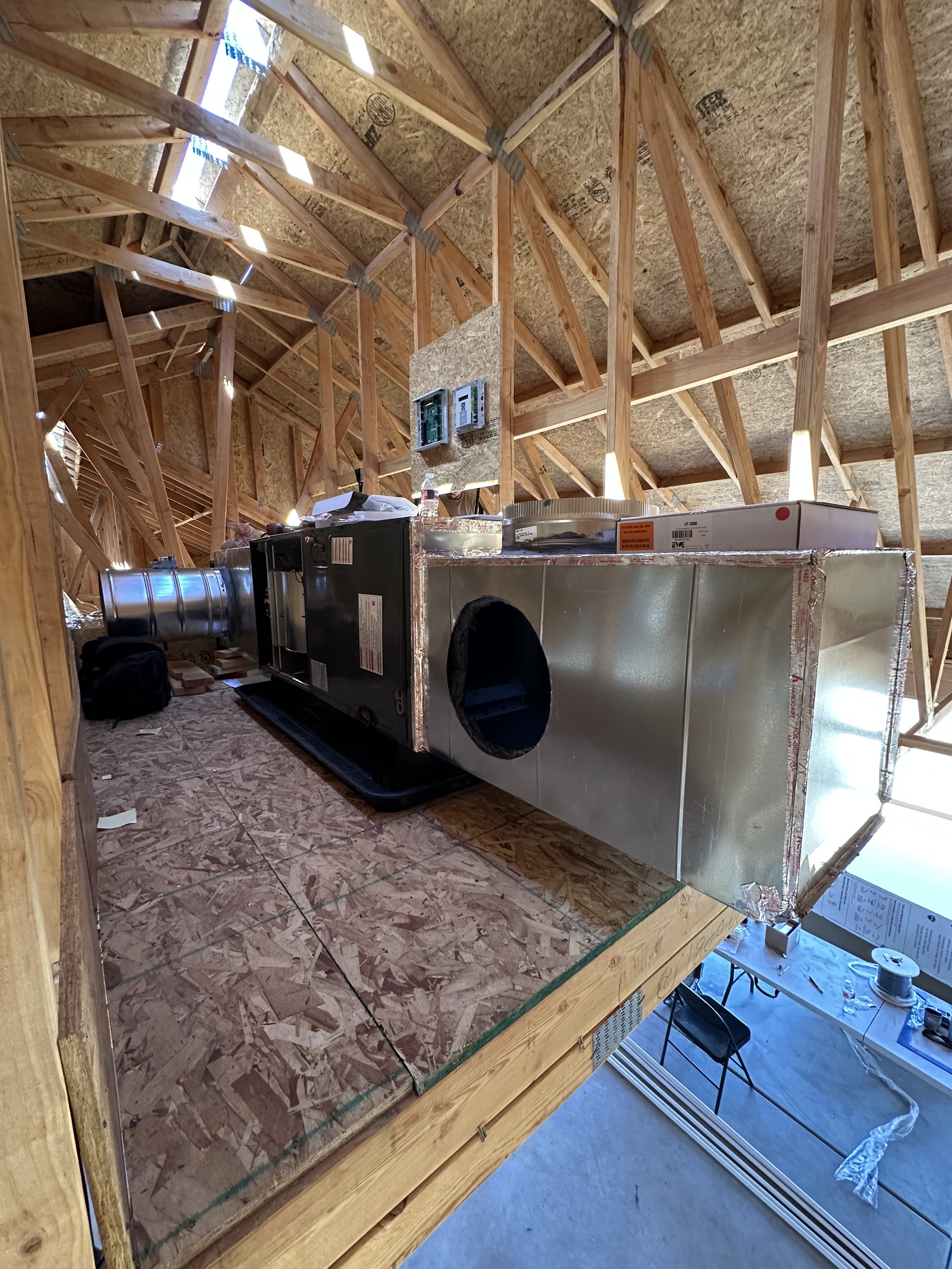 Construction site with a wooden framework, insulation, and a partially installed metallic HVAC unit, with tools and materials scattered around.