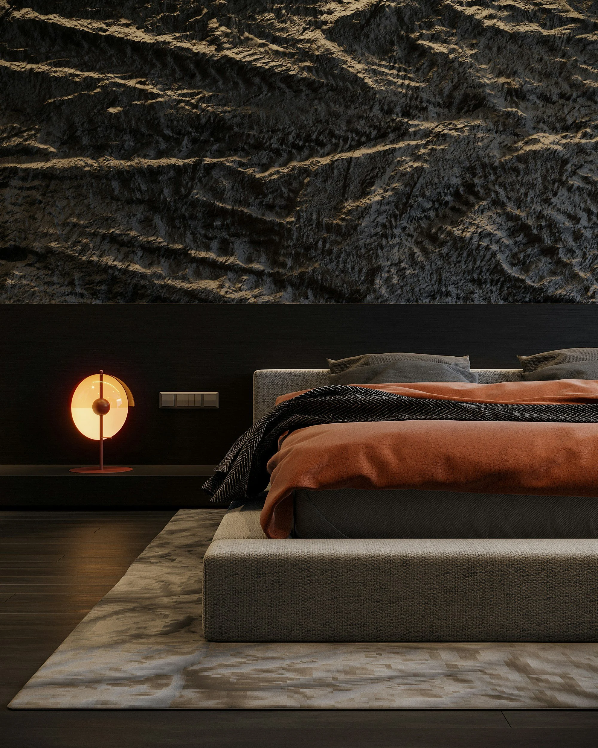 A modern bedroom with a textured black wall above the bed, a beige upholstered bed frame, rust-colored bedding, and a black patterned blanket. There is a glowing, amber-colored bedside lamp on a floating shelf and a light-colored rug on a dark wooden floor.