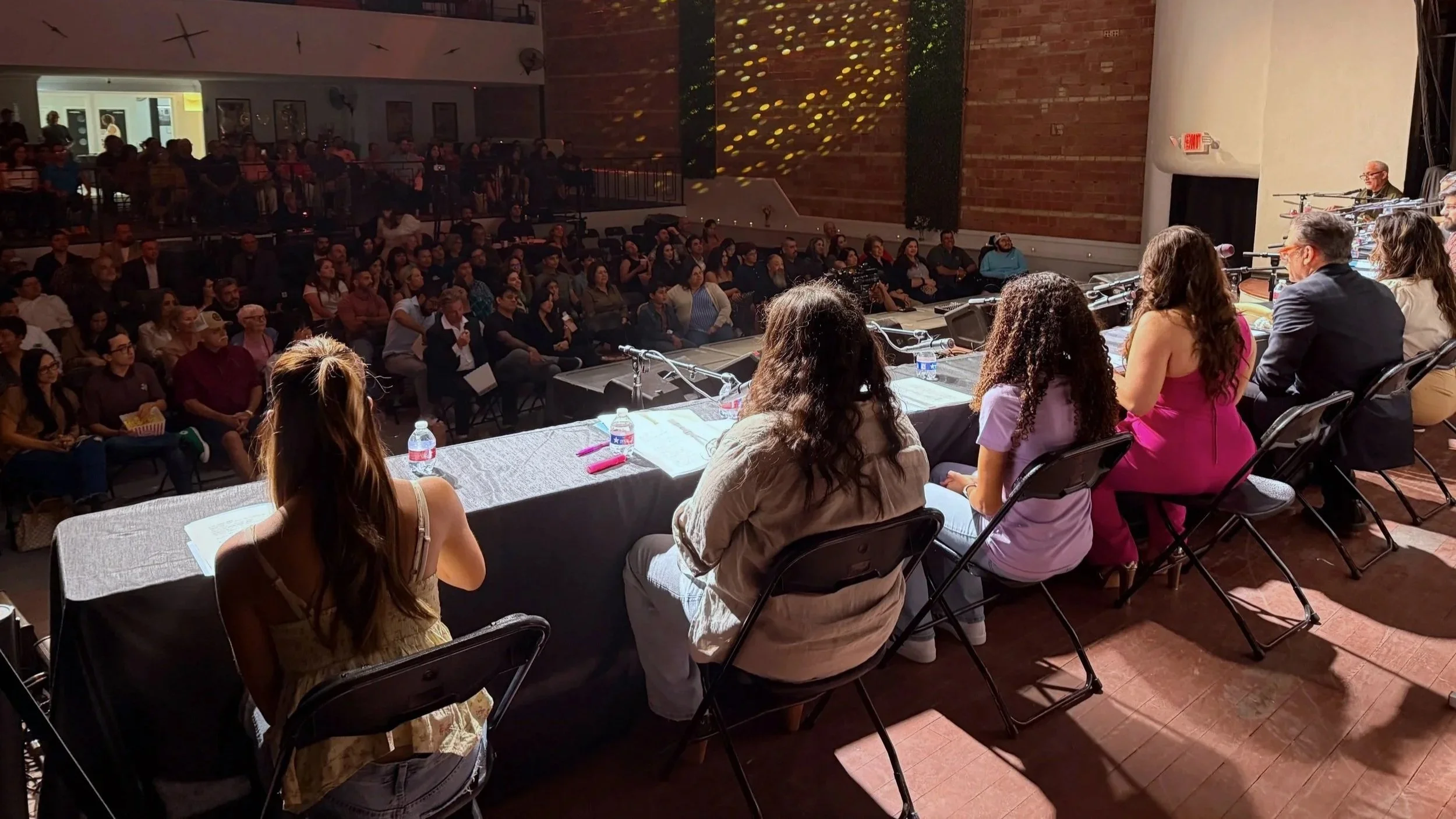 Panel of speakers seated at a long table addressing an audience in a large auditorium.
