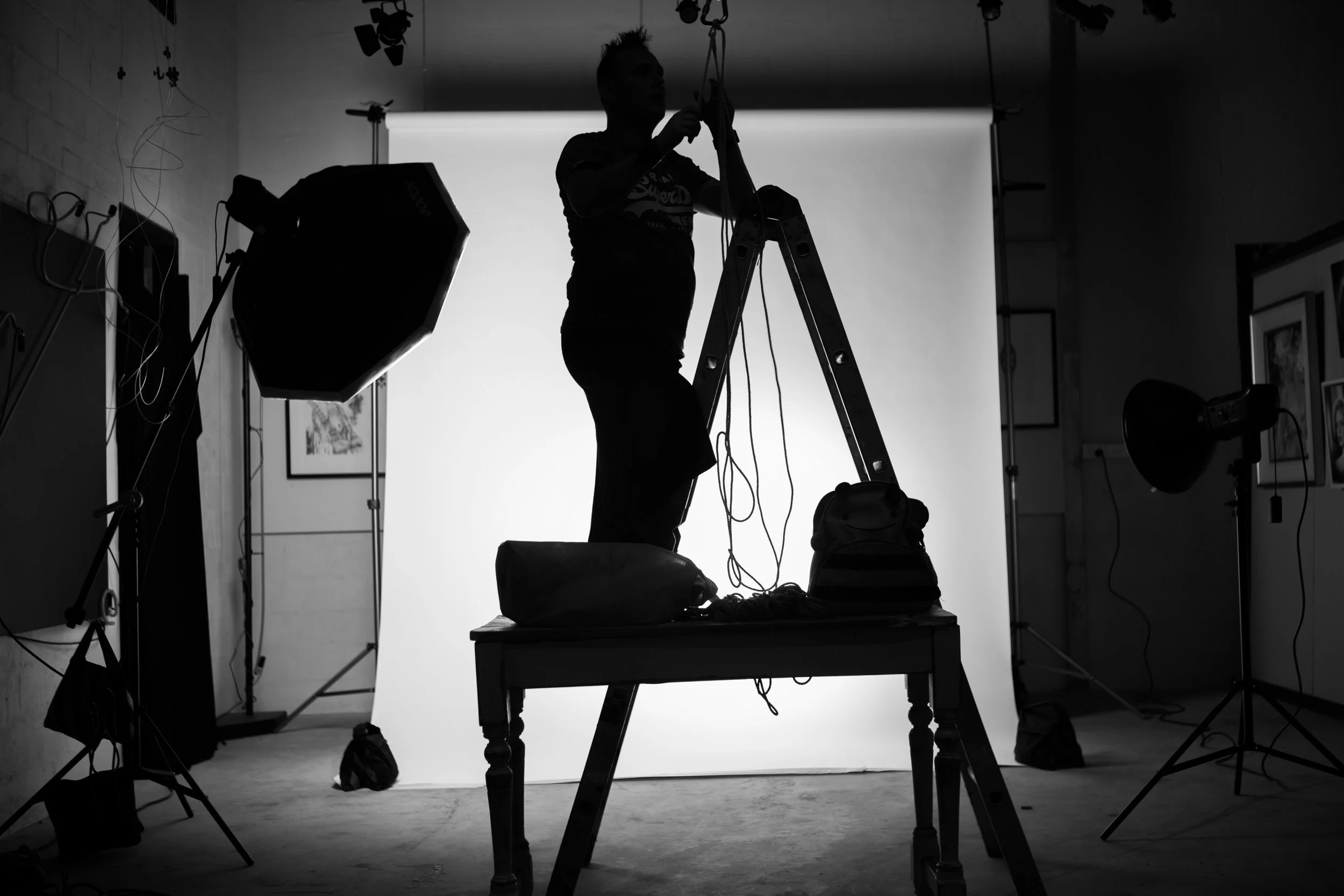 A person on a ladder adjusting lighting equipment in a photography studio.