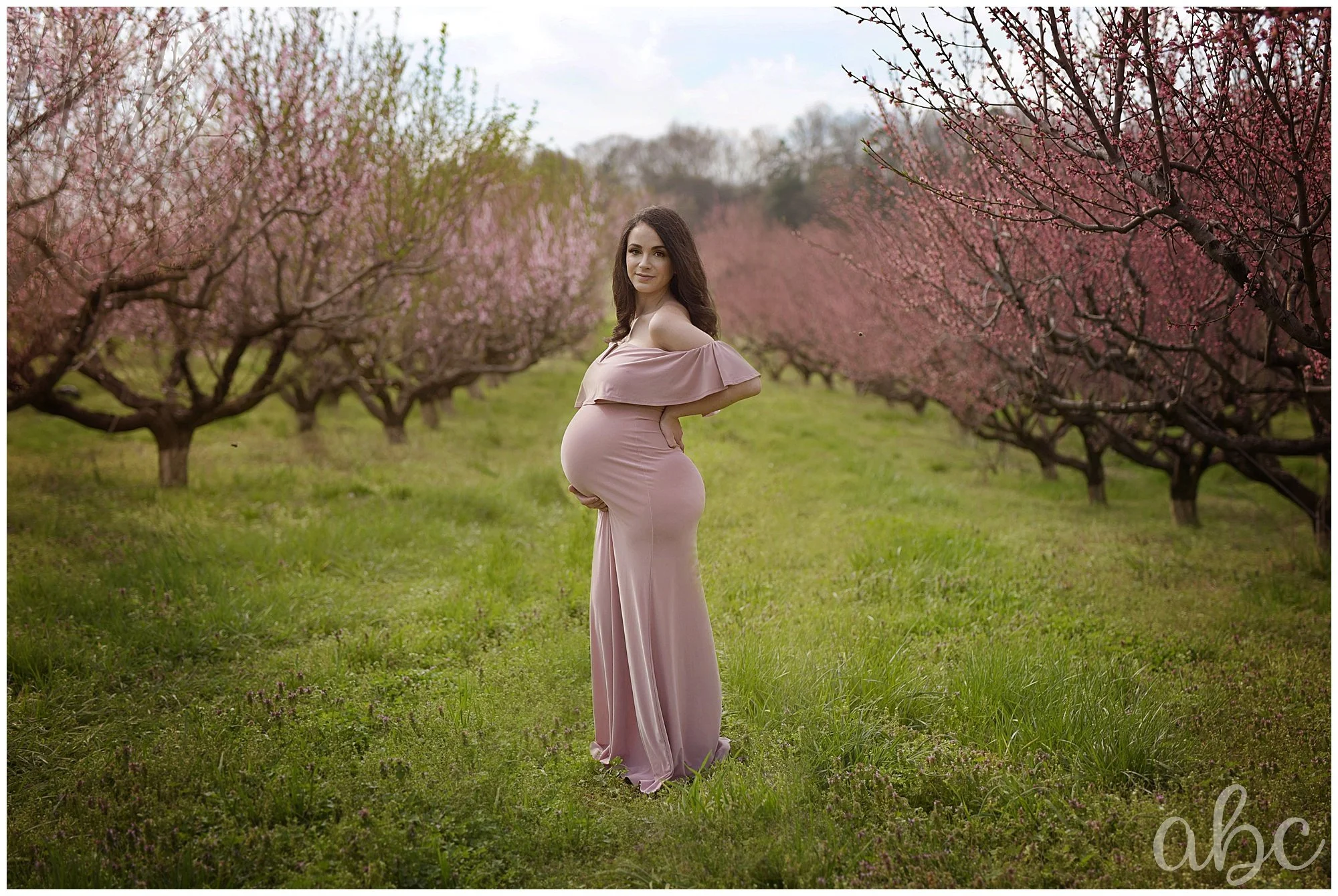 Chiropractor is pregnant and posing with her Roswell doula photographer in the cherry blossoms