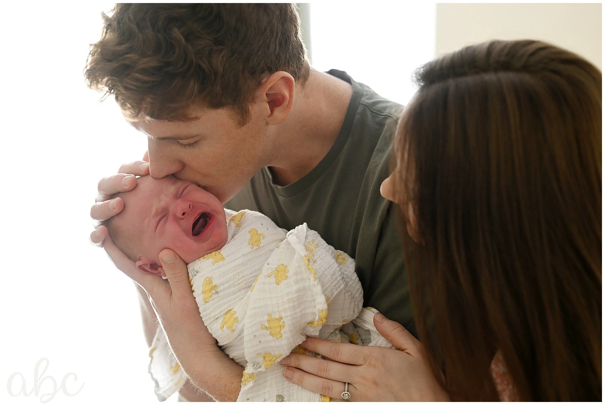 Dad kisses crying baby while the mom cuddles