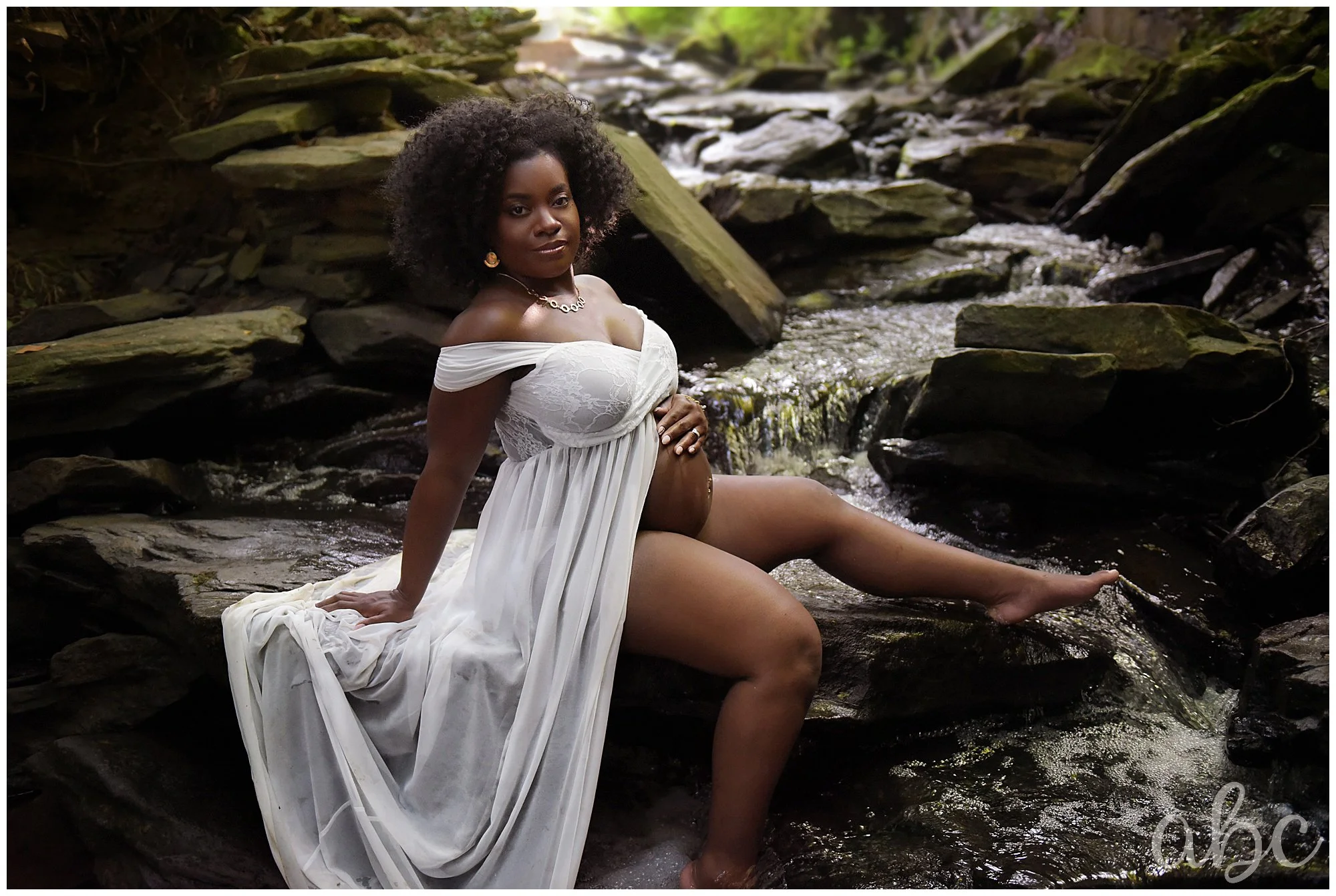 Woman poses near a waterfall in a white dress while Roswell doula Maegan Hall takes a photo