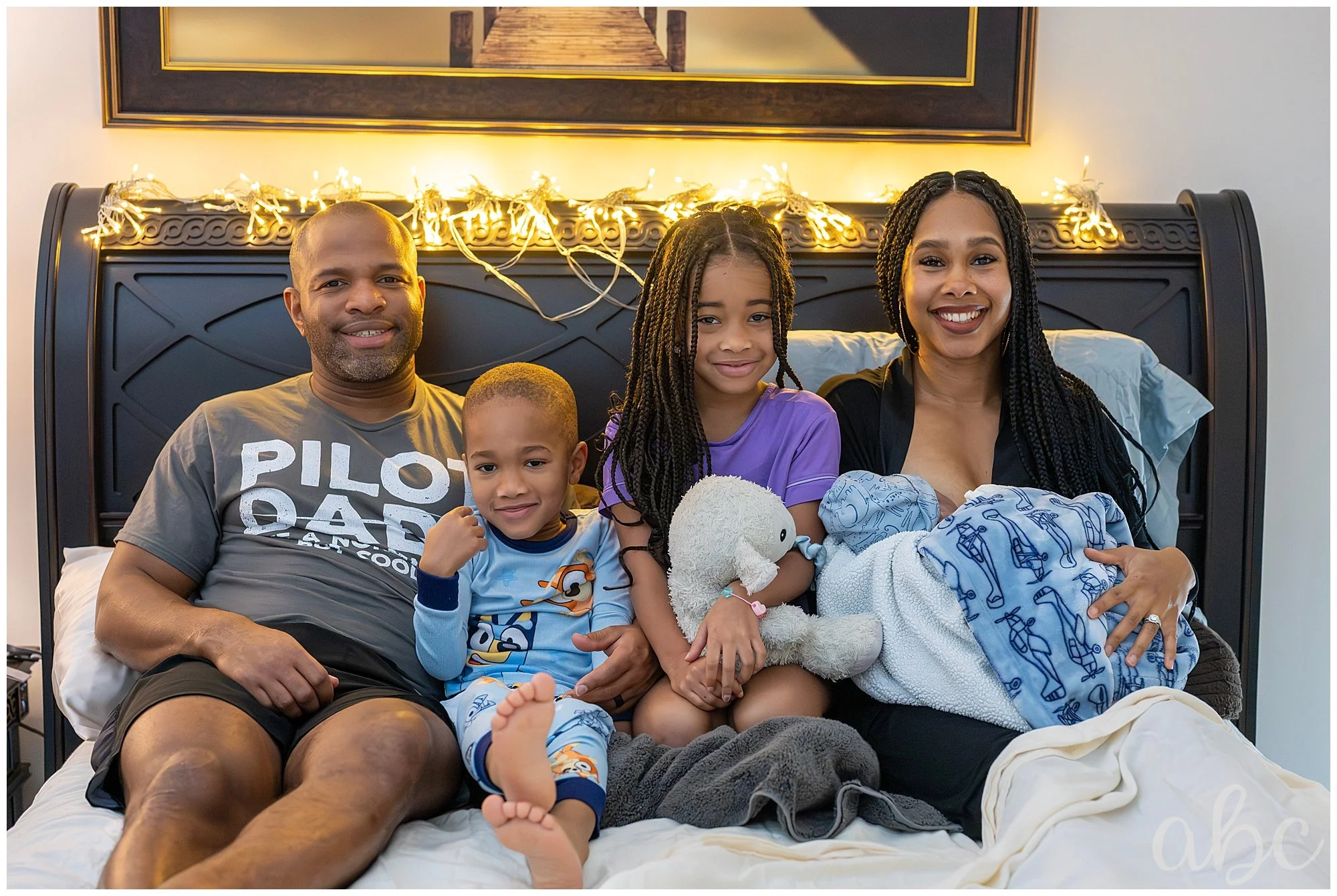 Family cuddles in the bed with new baby after home water birth. Photo by Atlanta Doula Photographer