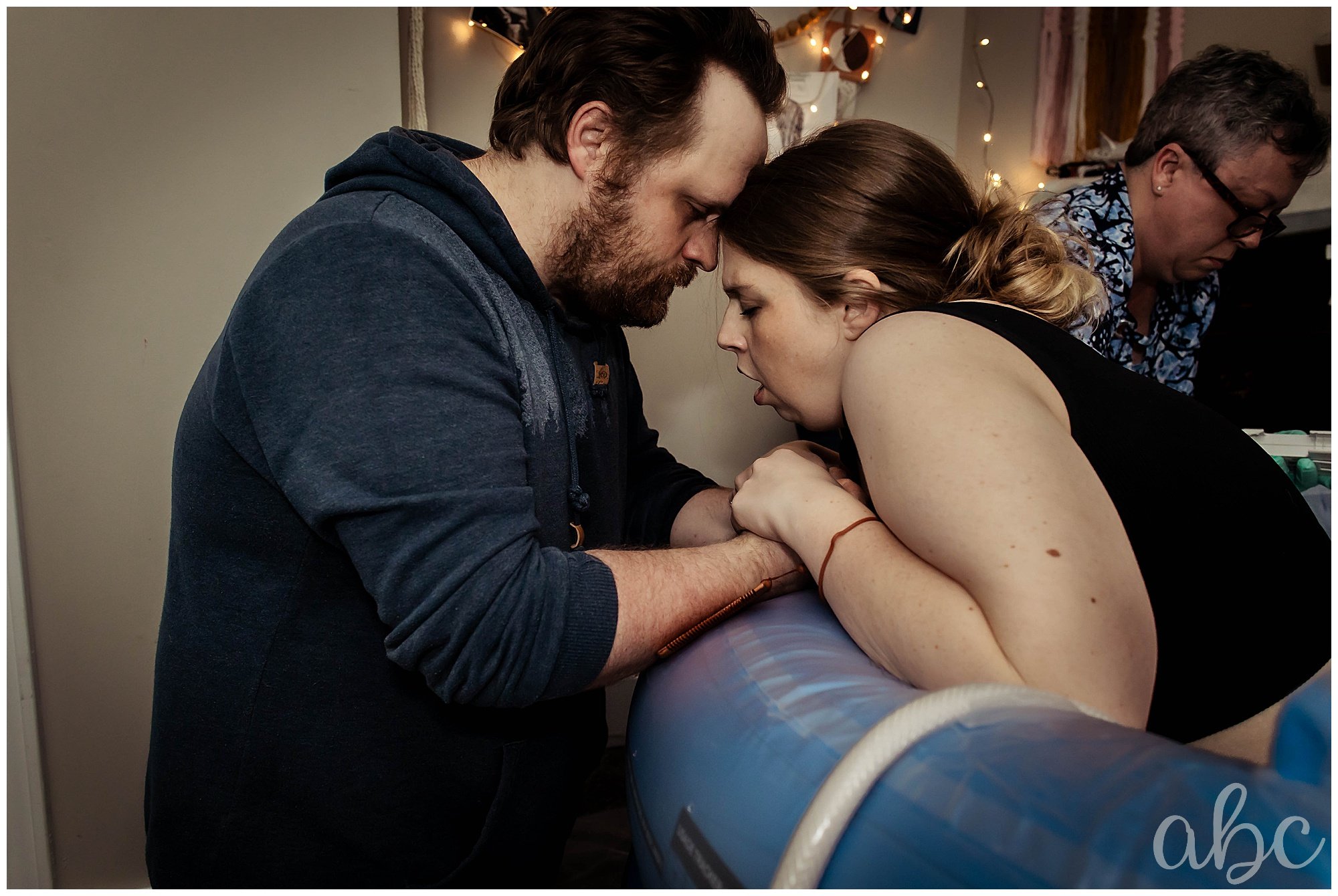 Dad holds laboring mother in birth tub at home. Woodstock doula coaches