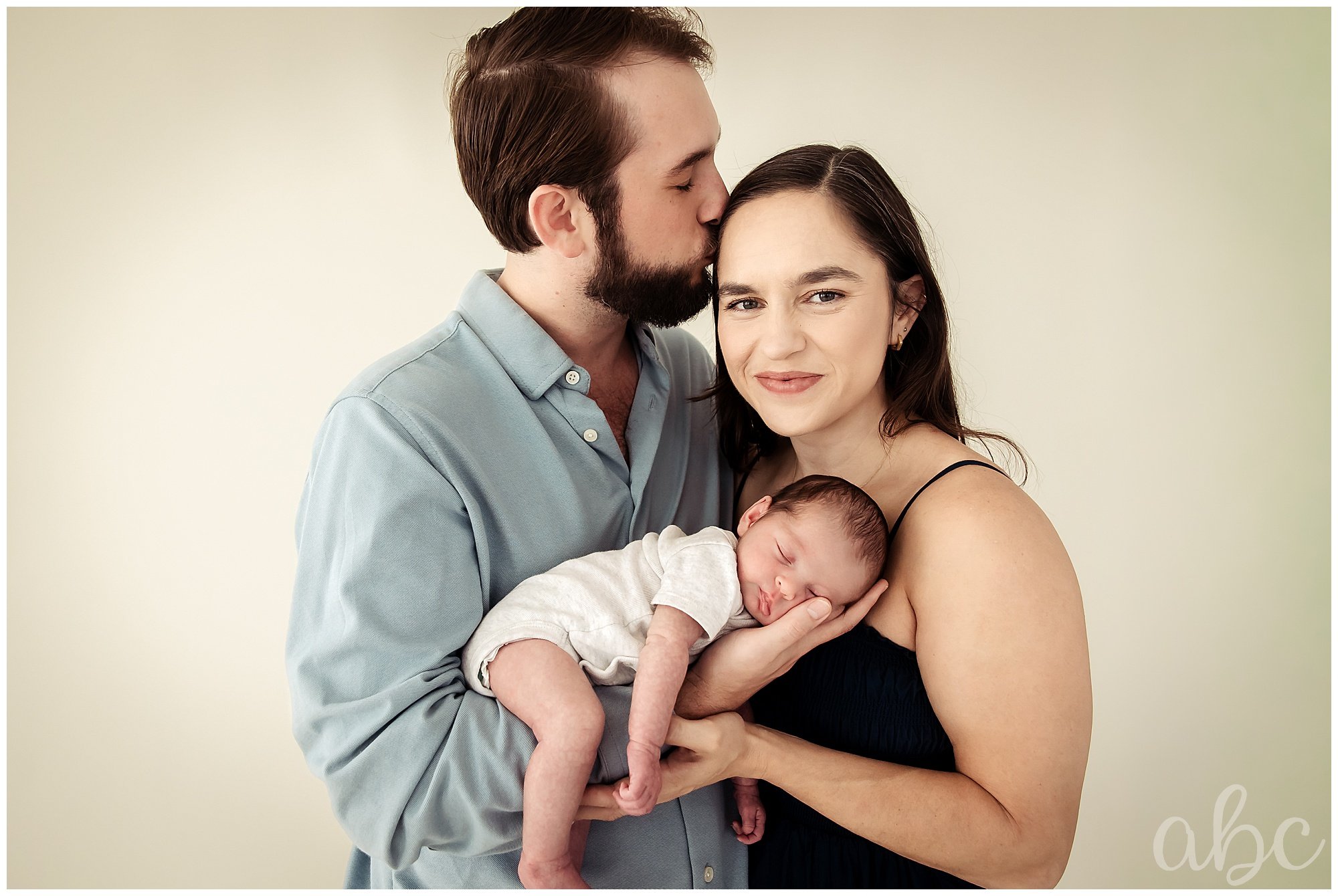 Father holds his baby and kisses his wife on the forehead
