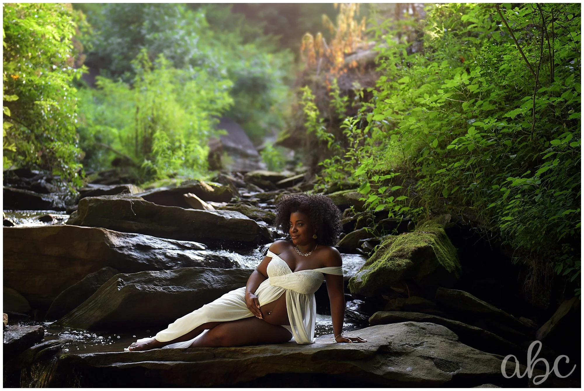 Pregnant woman poses on a rock while her doula takes a photo