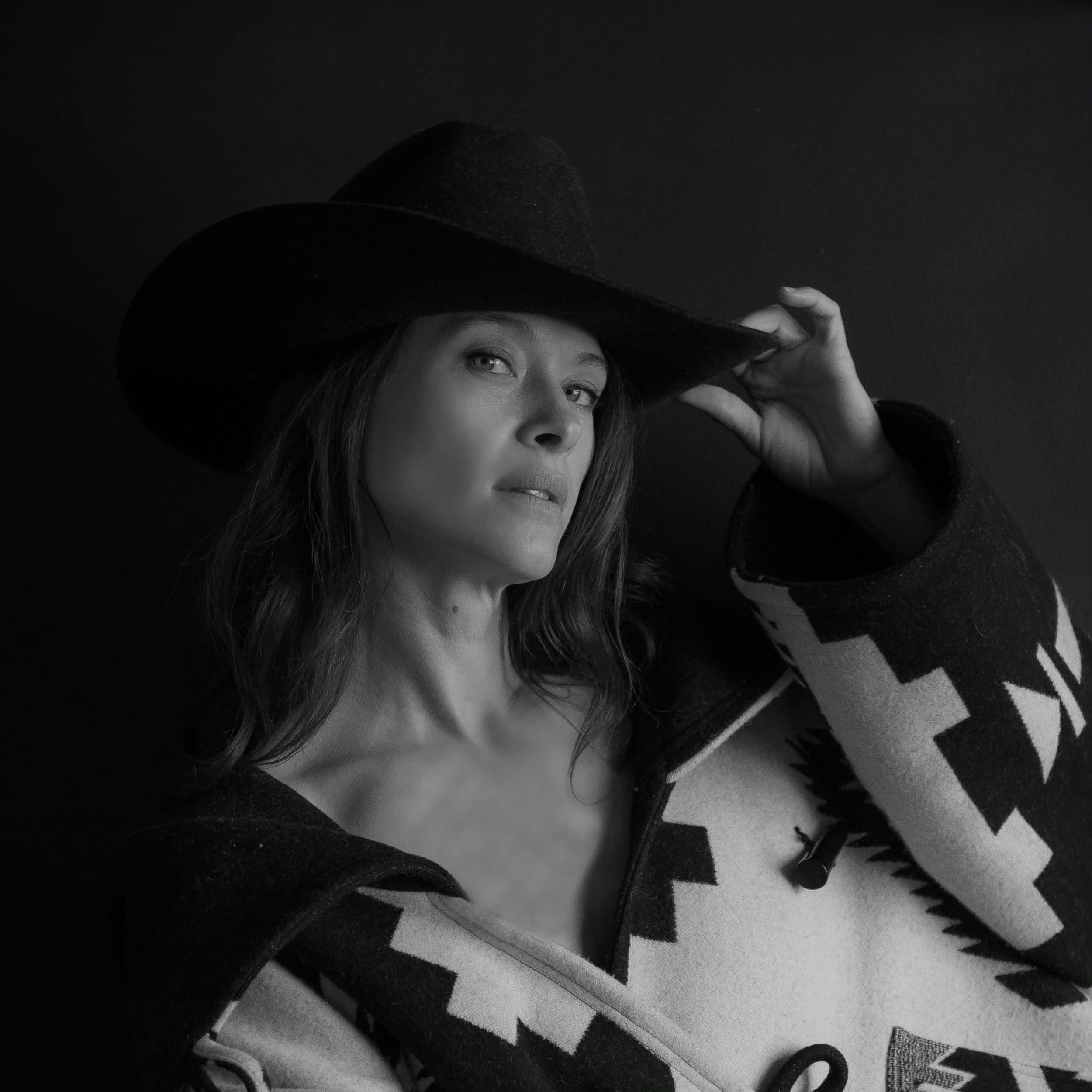Black and white photo of a woman wearing a wide-brimmed hat and patterned poncho, looking at the camera.