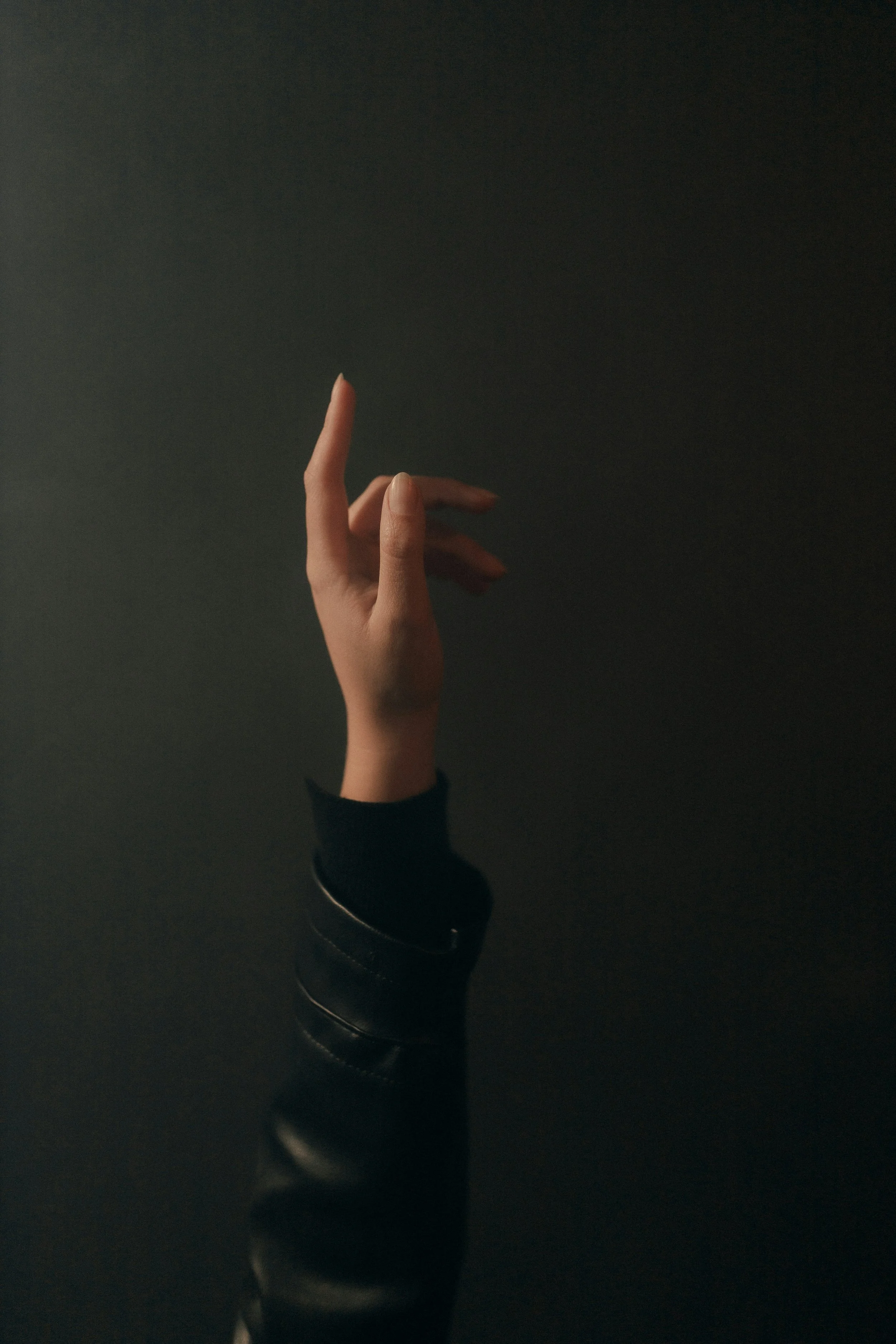 A person's hand with fingers turned upwards, wearing a black sleeve and a bracelet, against a dark background.