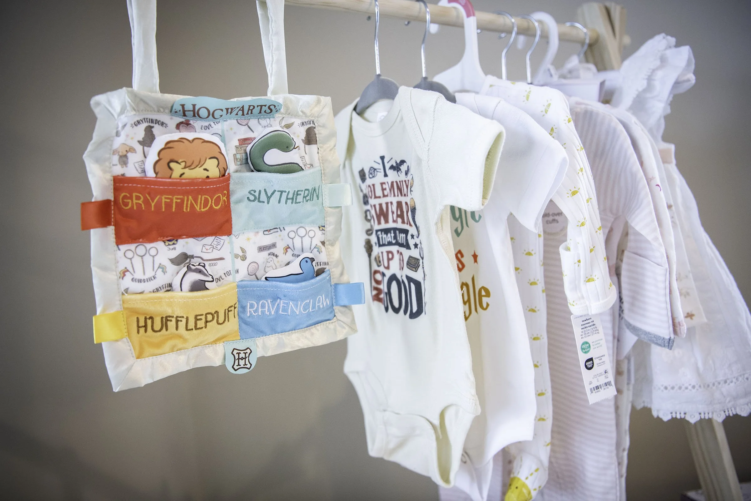Baby clothes hanging on a rack with a Harry Potter-themed fabric organizer in the foreground.