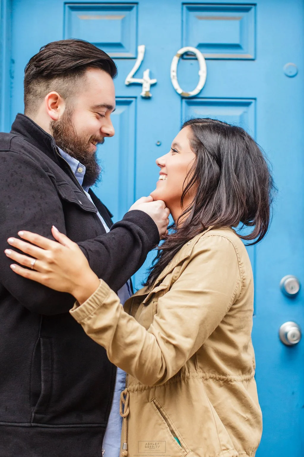 A man and woman standing close in front of a blue door with the number 40, smiling and looking at each other affectionately.