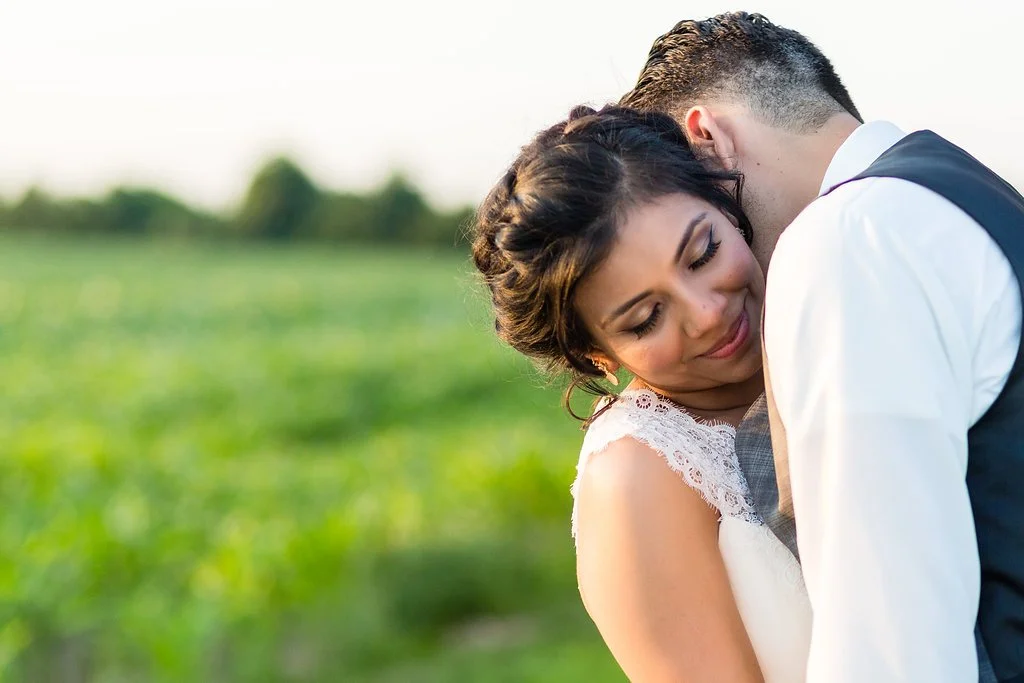 Close-up of a couple embracing outdoors, the woman resting her head on the man's chest with a gentle smile, in a green field during daytime.