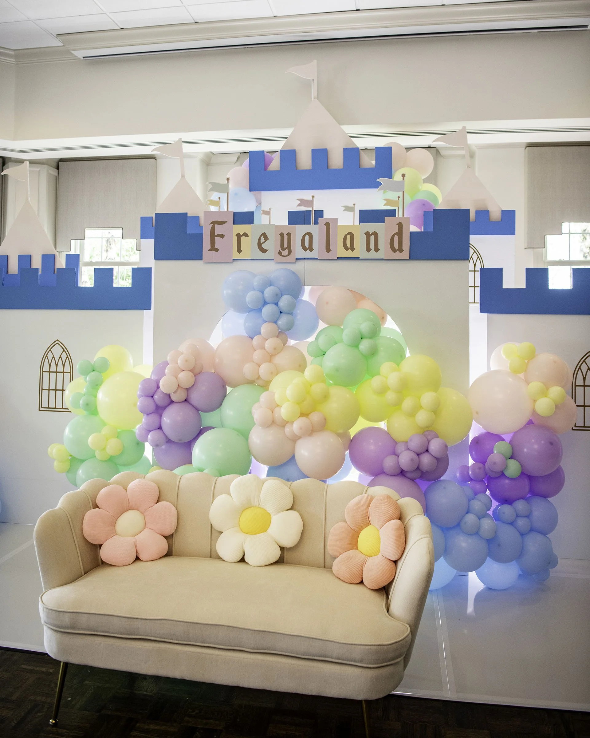 Colorful balloon decorations resembling a castle with a sign reading 'Freyaland,' and a pink sofa with flower-shaped pillows in front.