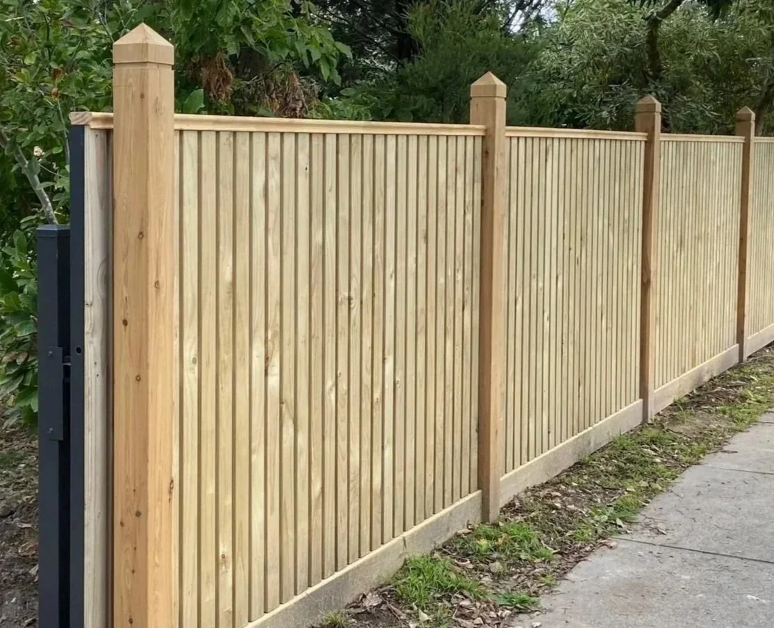 A newly installed wooden privacy front fence along a sidewalk with green foliage in the background.