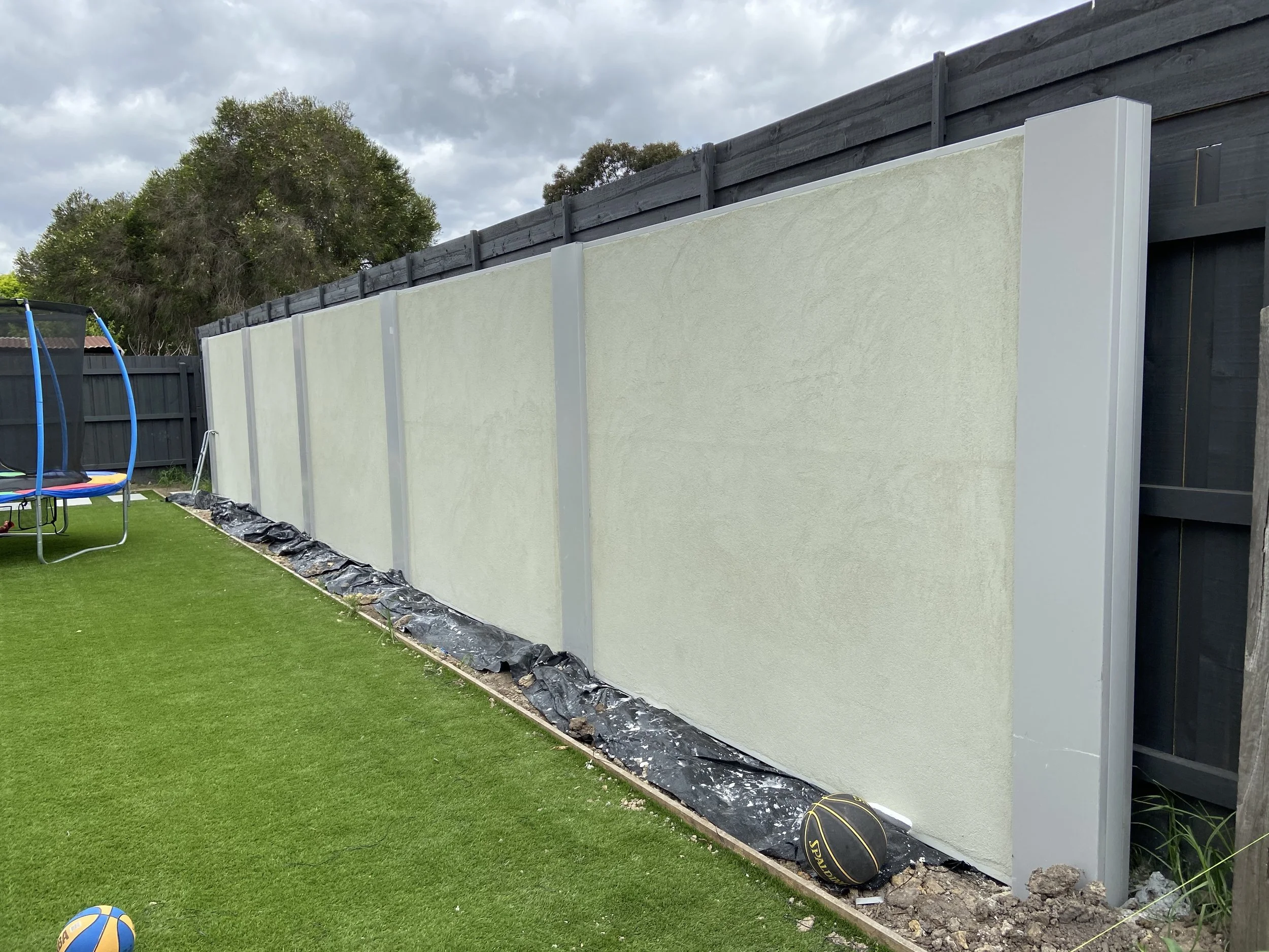 Backyard with a newly built beige privacy fence, a trampoline, a football, and artificial grass.