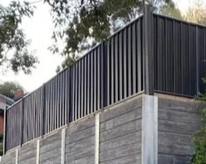 Close-up of a black metal fence attached to a concrete wall with trees in the background