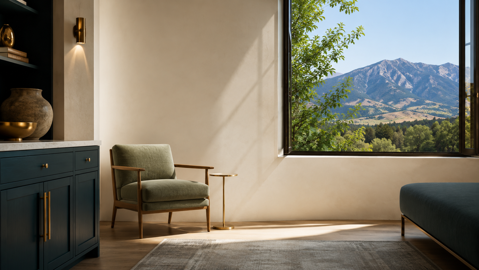 A living room with a large window showing a mountain landscape, an olive green armchair with wooden arms, a small side table, a blue cabinet with gold handles, decorative objects on a shelf, and a beige wall with a wall sconce.